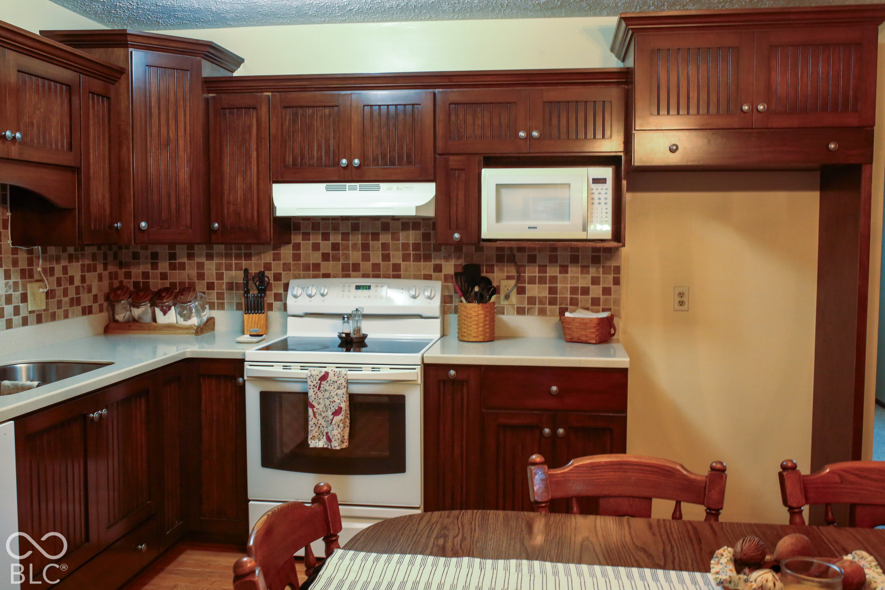Kitchen with dark wood cabinets, tiled backsplash, white appliances, and a dining table in the foreground.