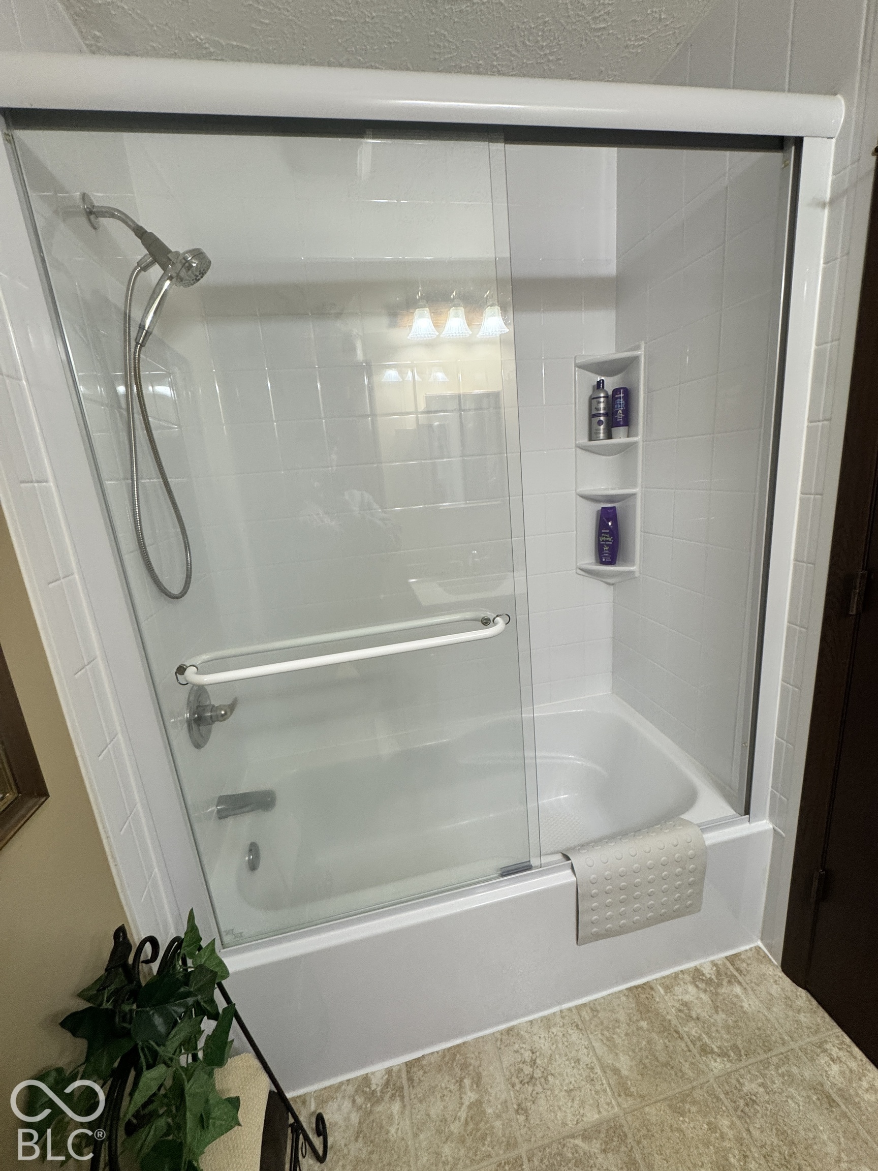 Bathroom bathtub with glass shower doors, handheld showerhead, and built-in corner shelves.