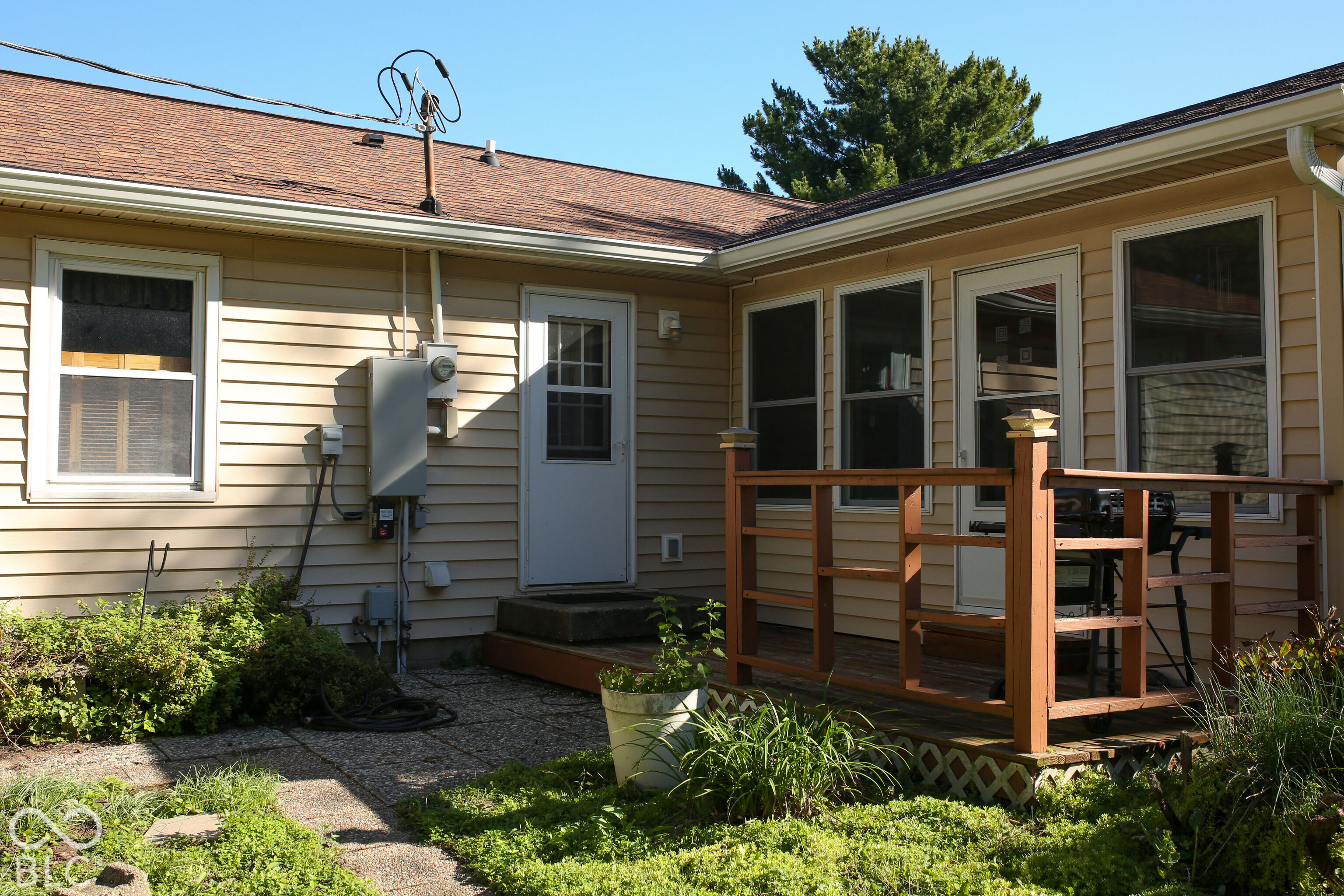House’s rear exterior with a raised wooden deck, patio chairs, and a garden path.