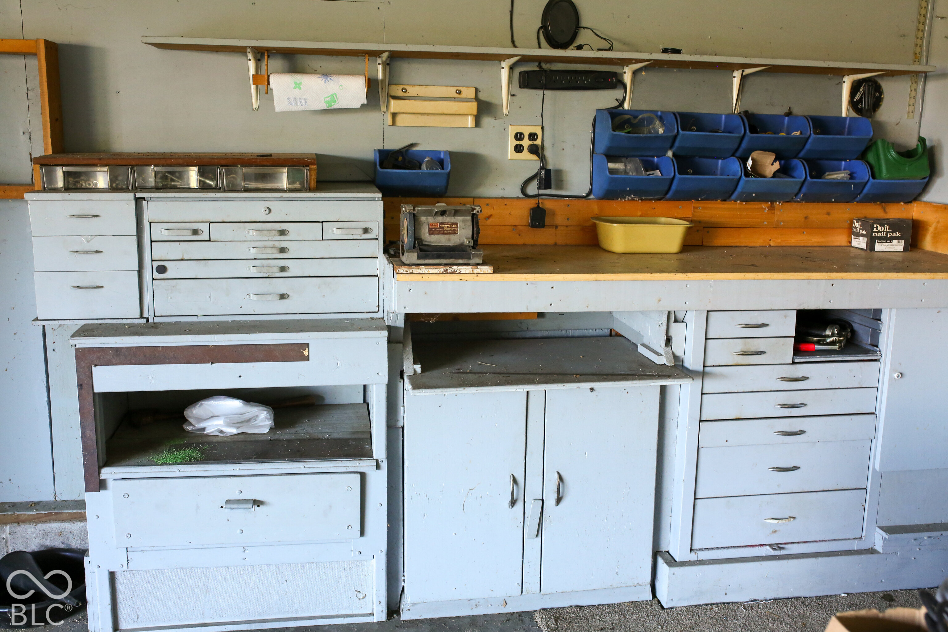 Garage workshop with a built-in workbench, extensive drawers, blue parts bins, and a bench grinder.
