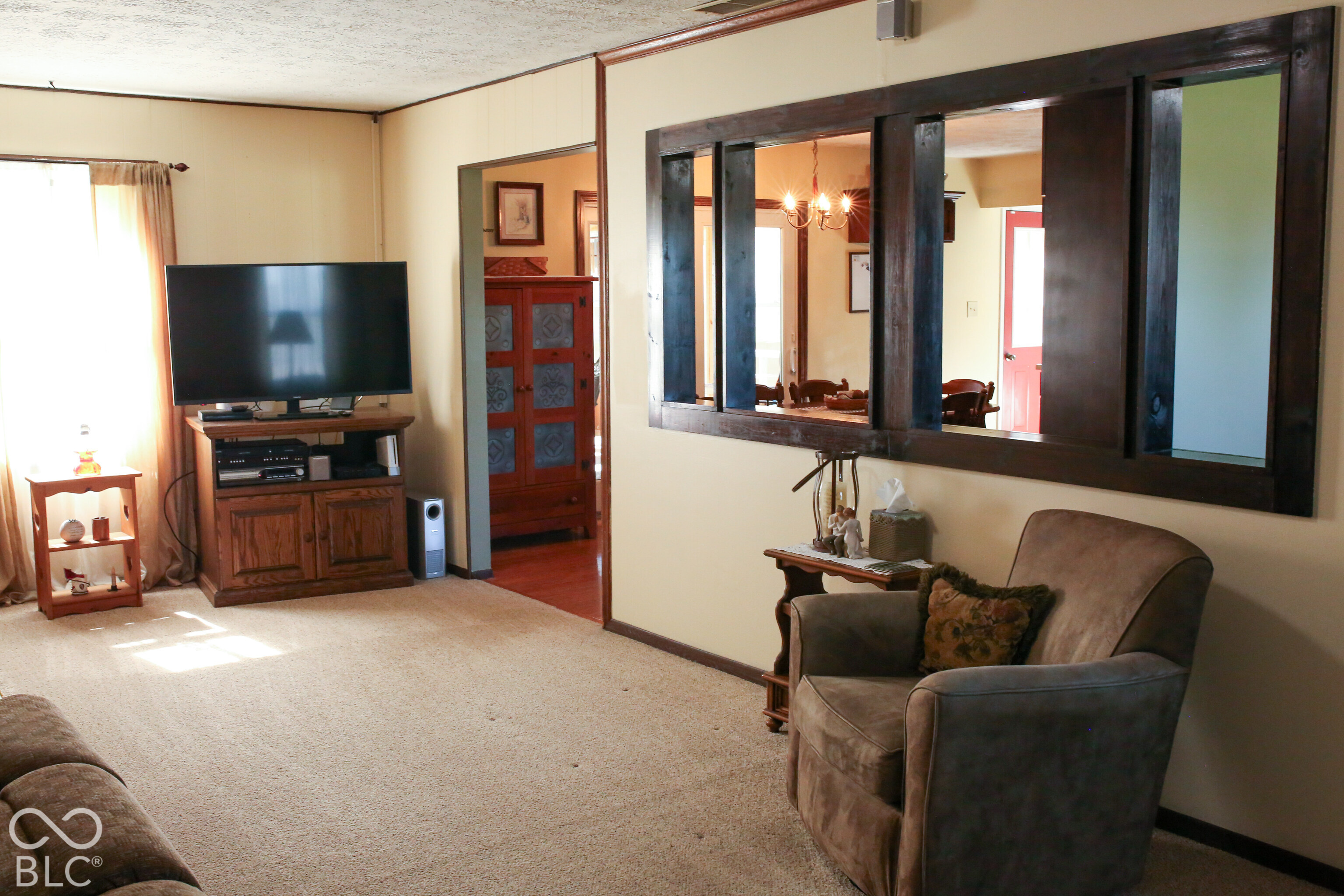 Living room with beige carpet, wooden media cabinet, and a large dark-wood opening to the dining room.