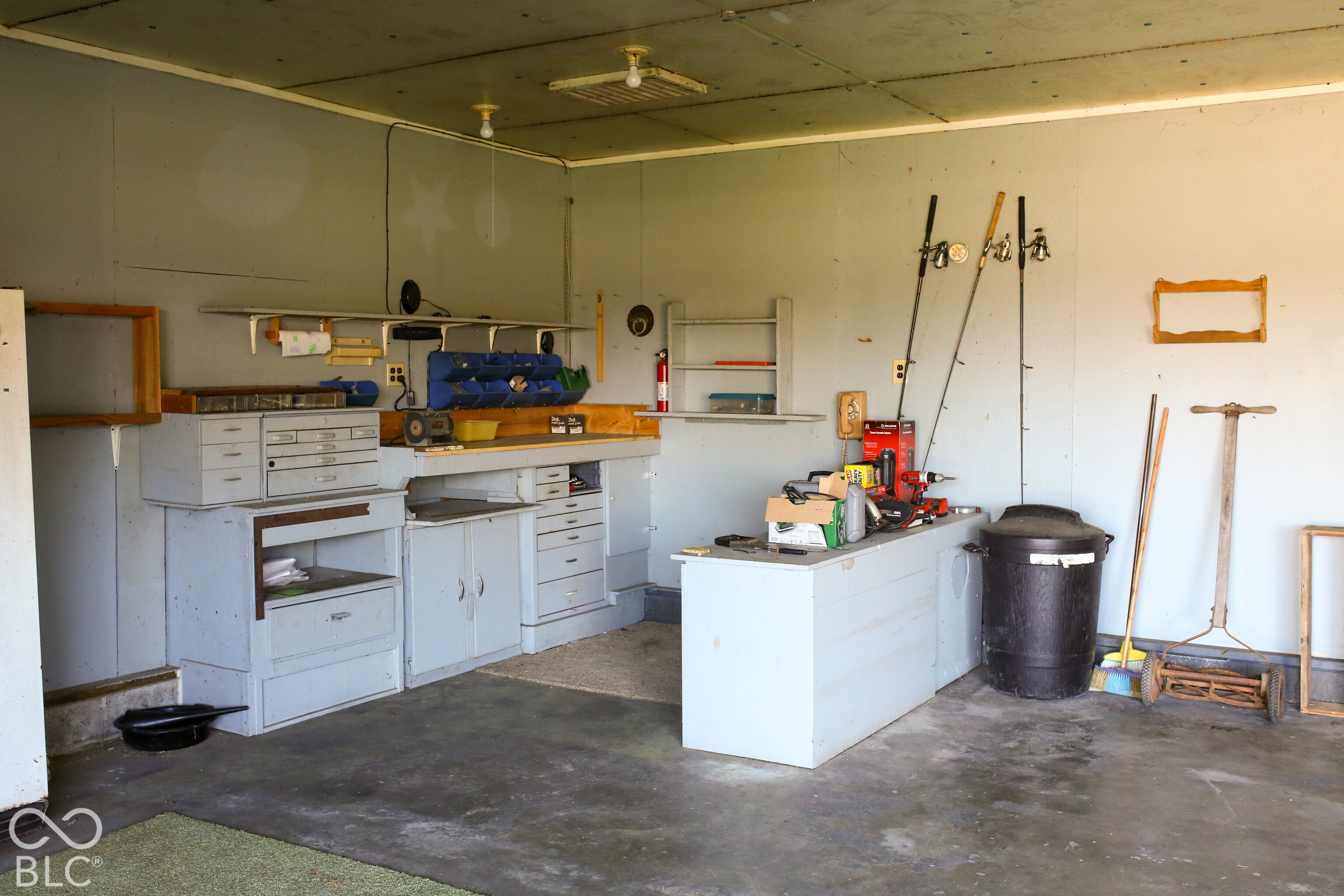 Garage workshop with built-in cabinets, workbenches, fishing rods, and a freestanding table.