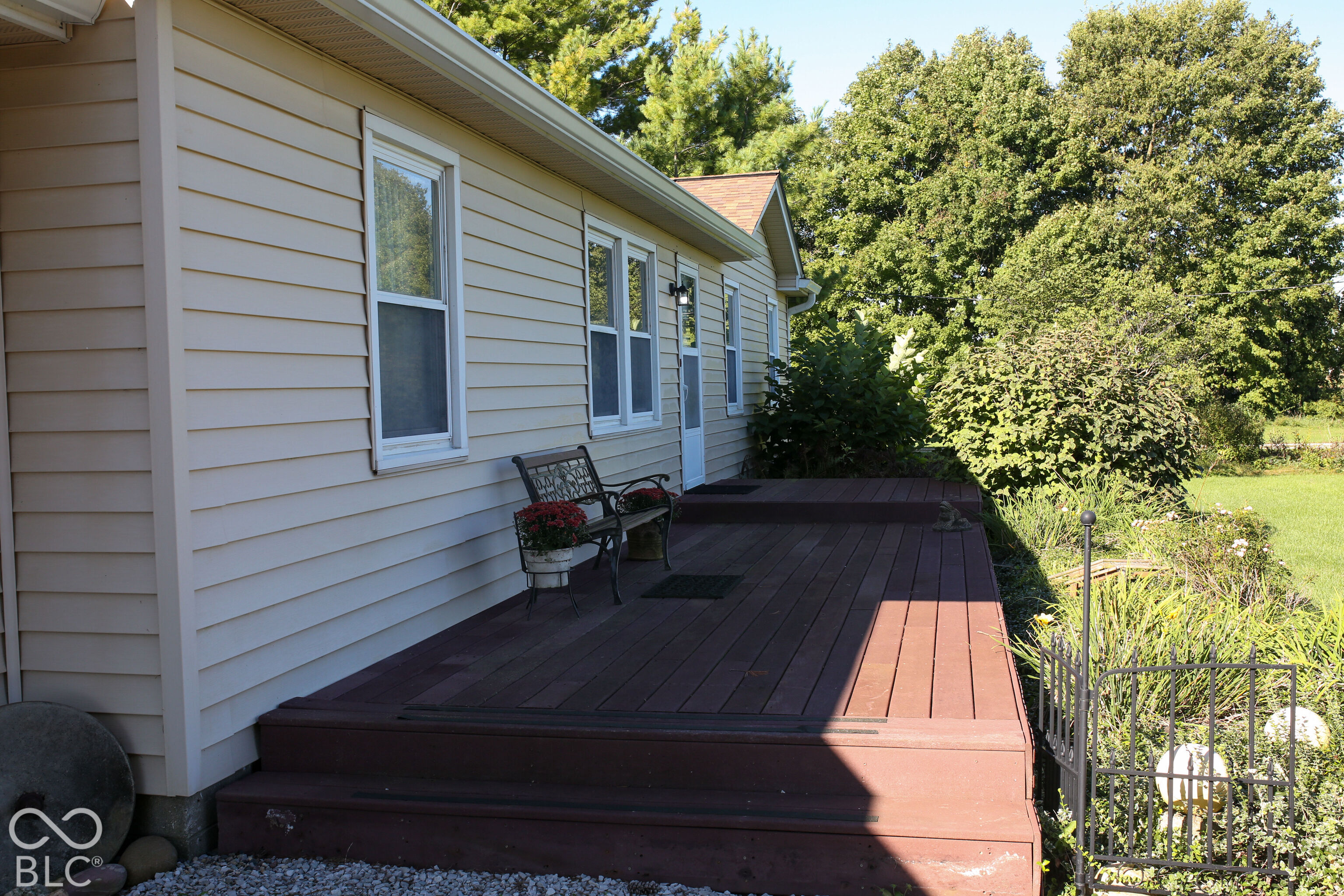 House side deck with dark wood steps, a bench, potted flowers, and a garden.