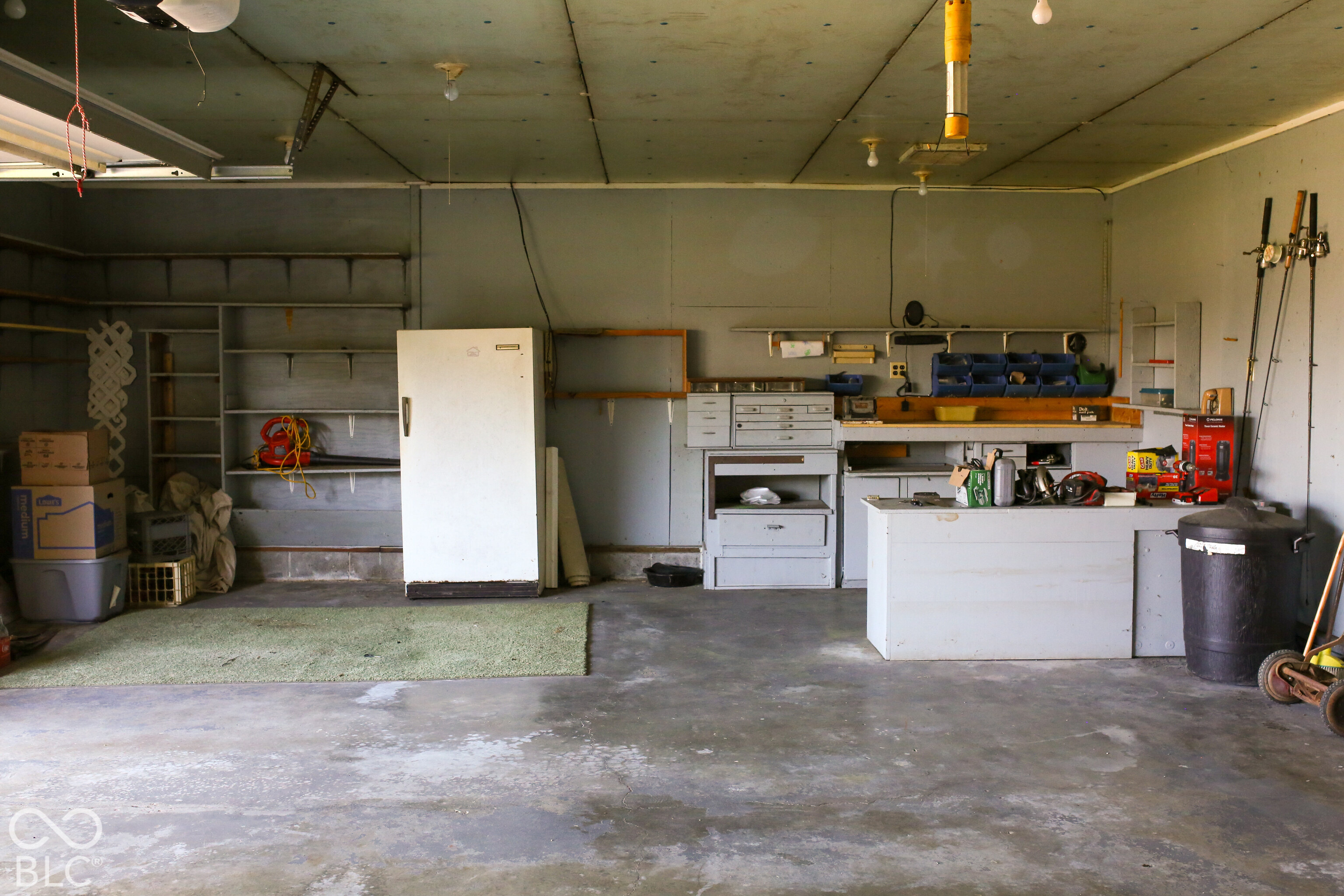Garage workshop with built-in workbenches and shelving, a refrigerator, and tools.
