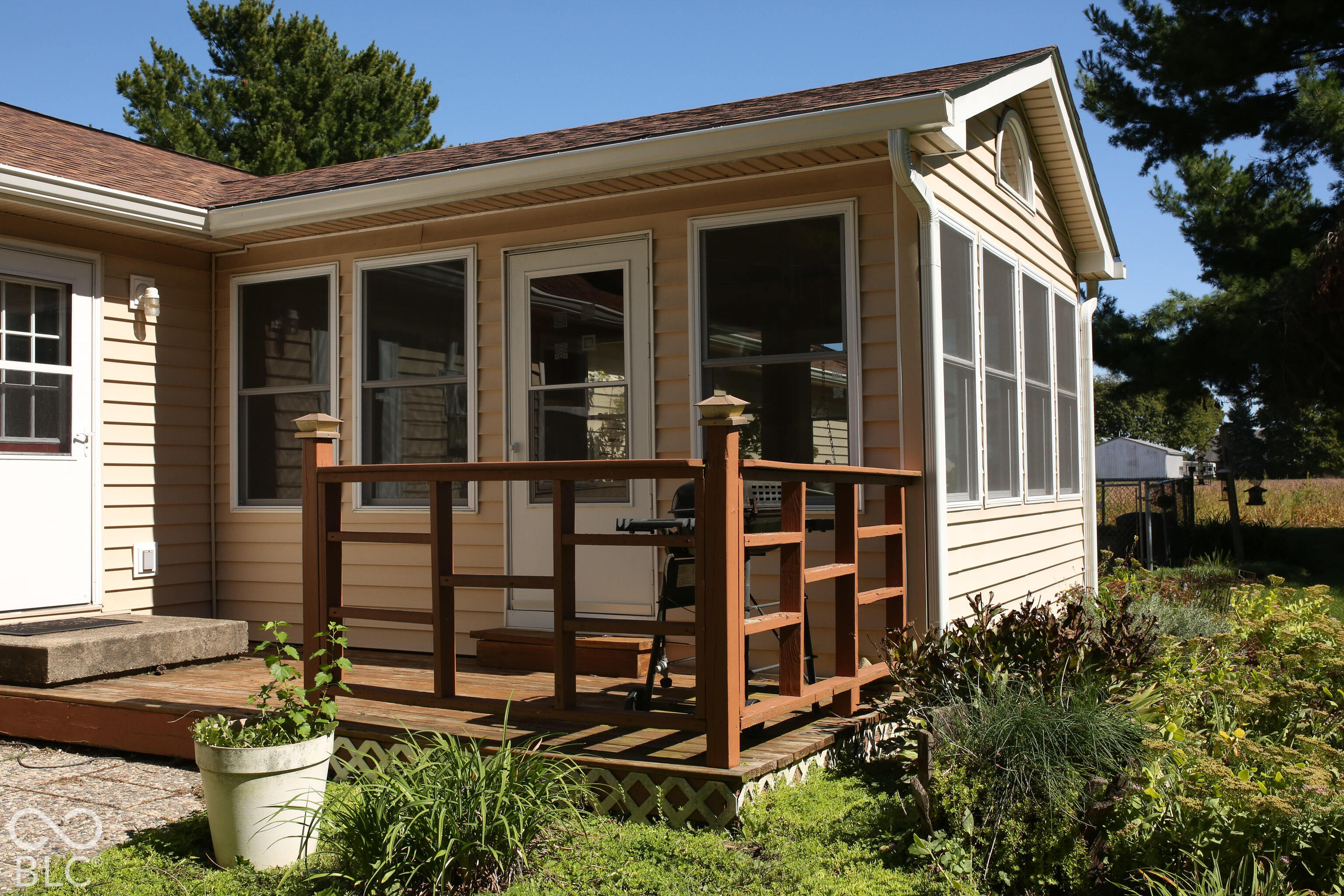 House rear with a raised wooden deck, large windows, and garden beds.