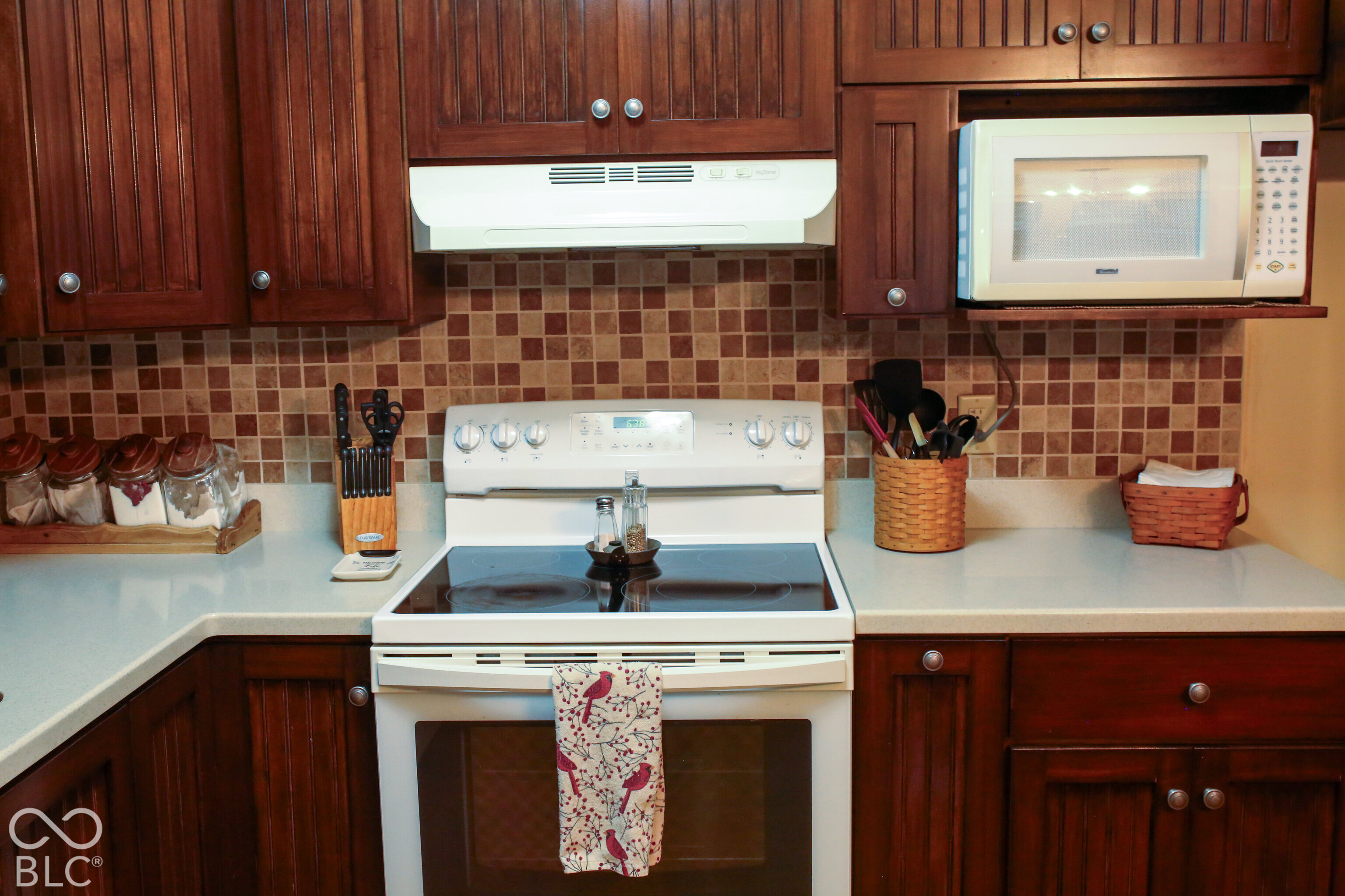 Kitchen with dark wood cabinets, tiled backsplash, white electric range, and built-in microwave.