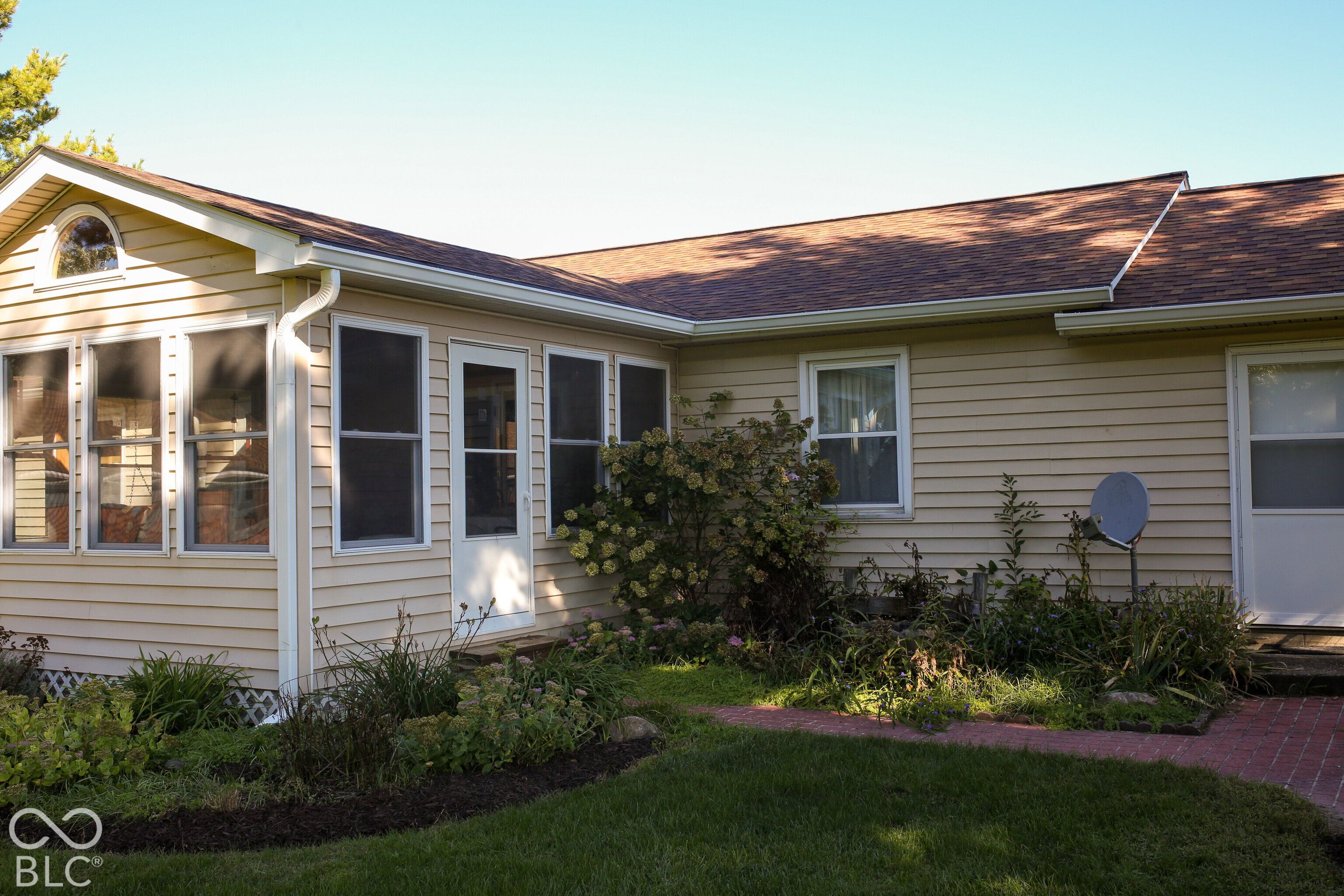 Beige-sided home exterior with a garden, screened windows, and a brick walkway.