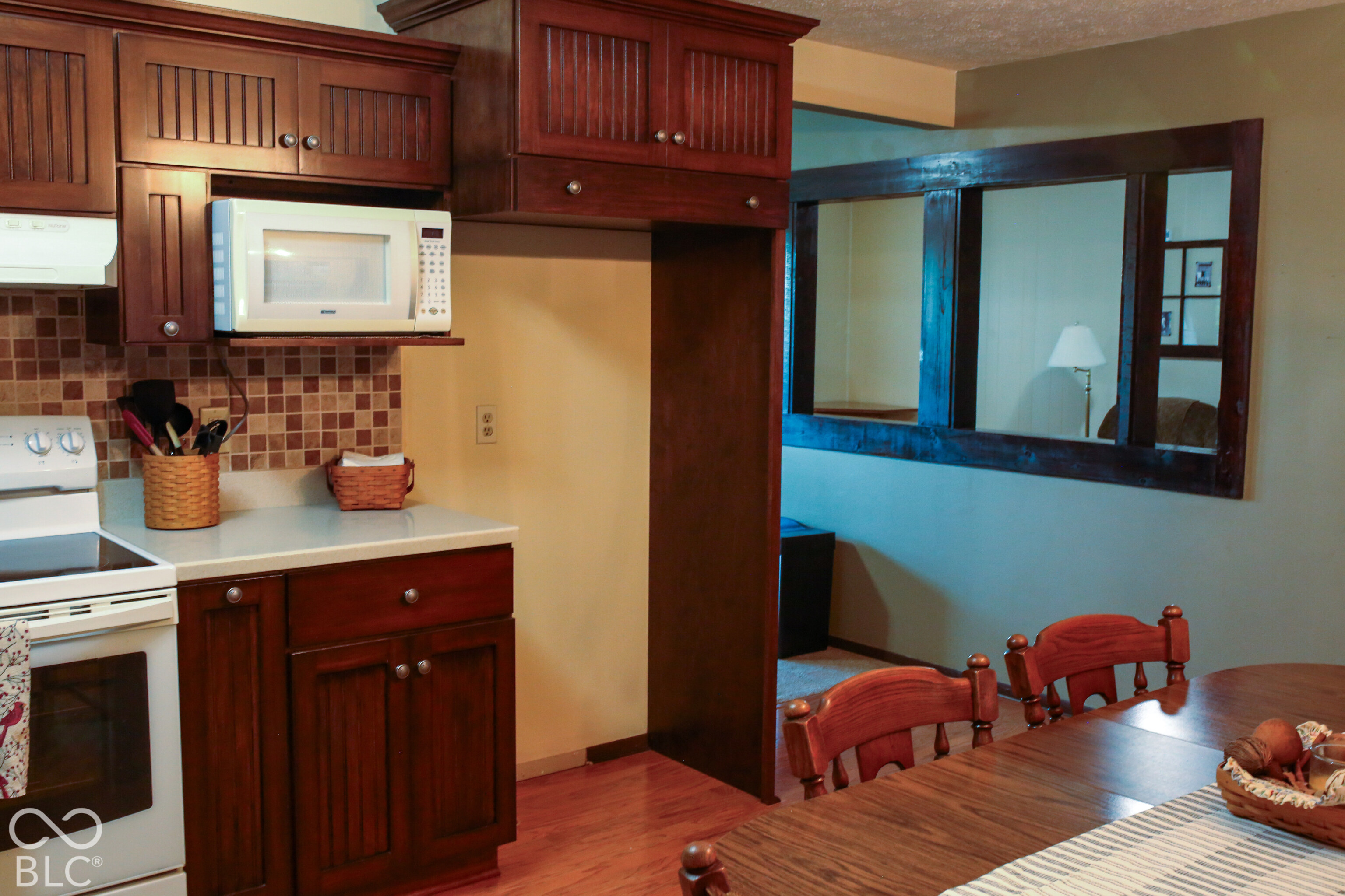 Kitchen with dark wood cabinetry, white appliances, and a wooden dining table beside a framed opening.