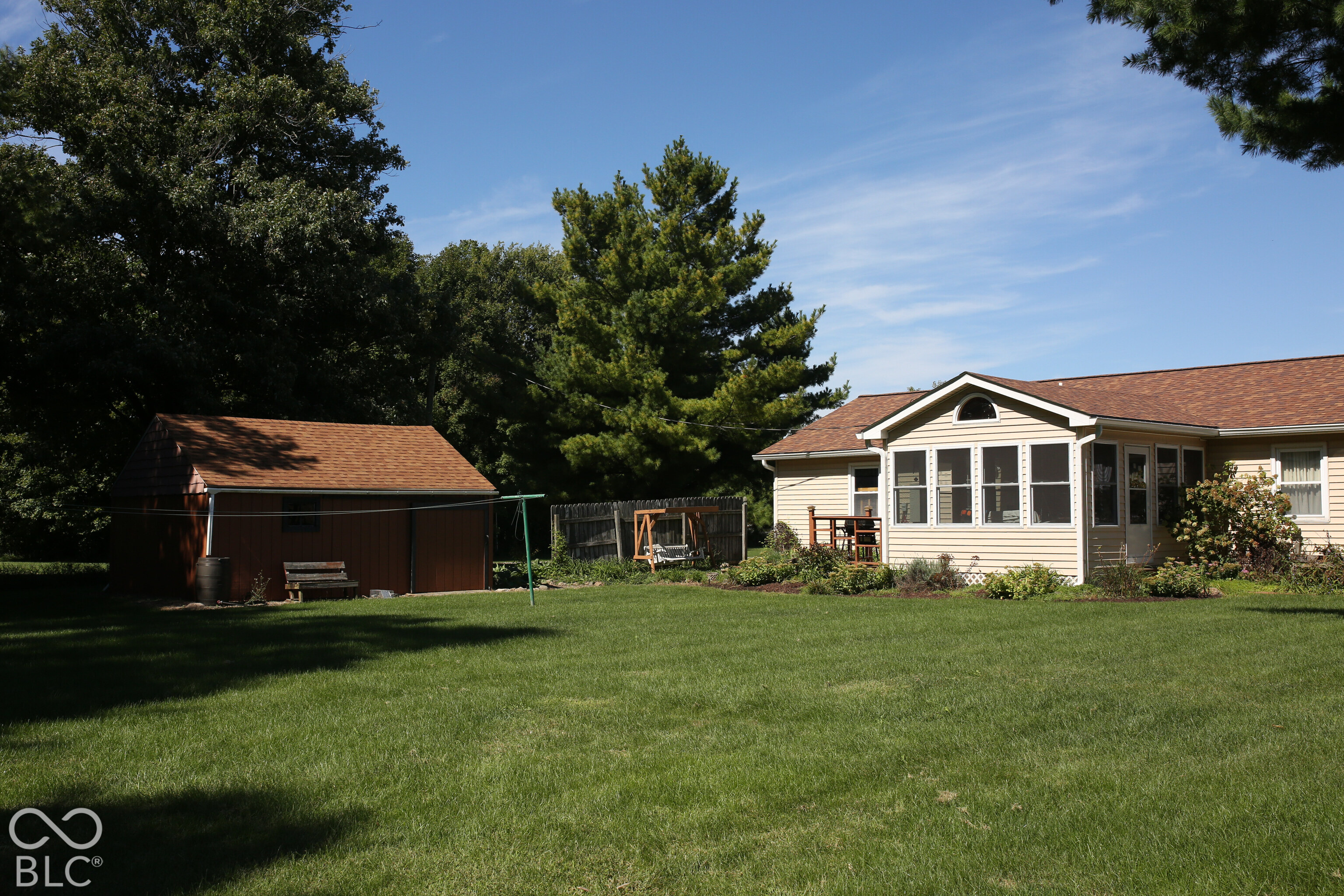 House’s rear screened porch beside a broad lawn, detached shed, and mature trees.