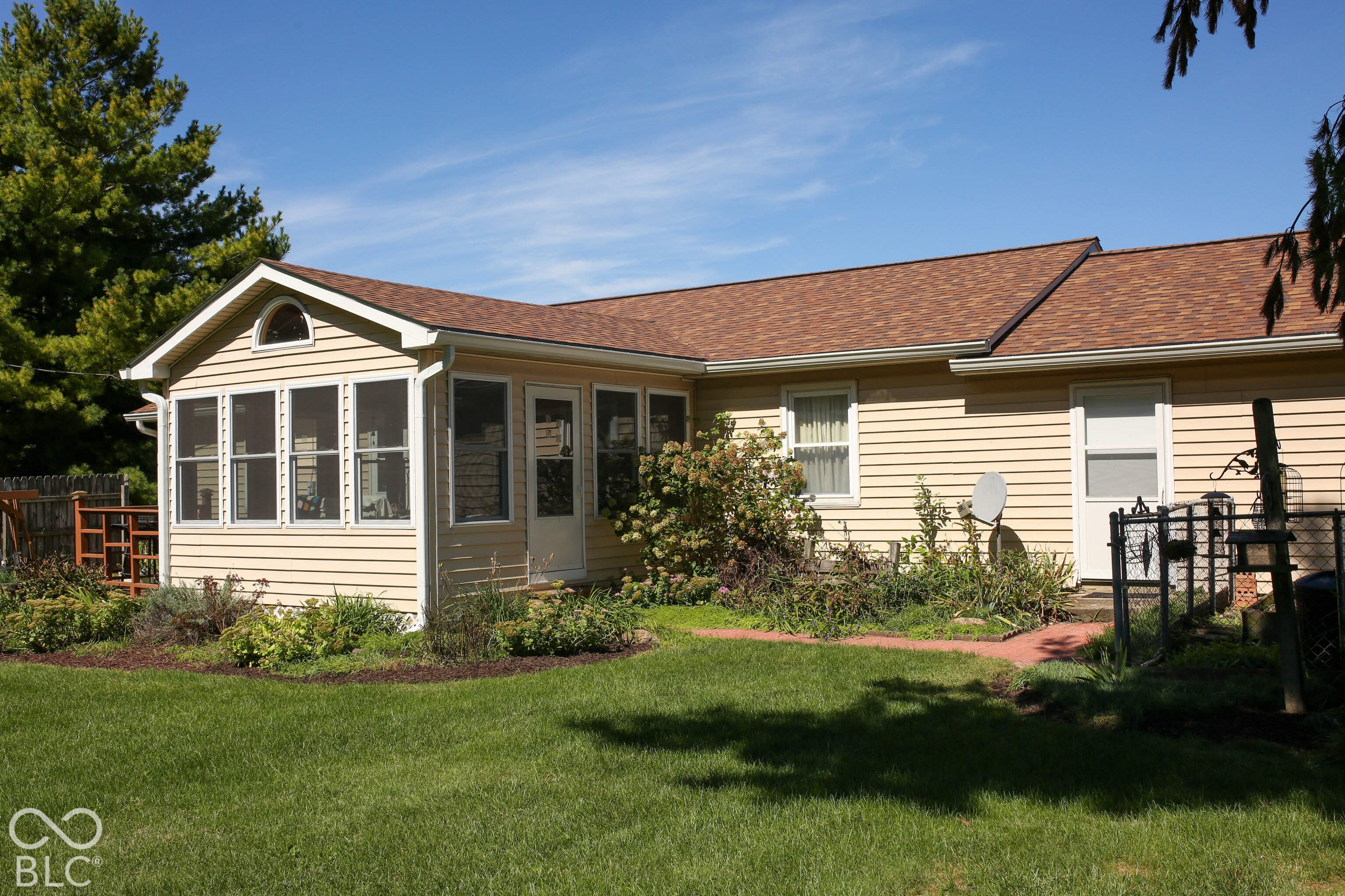 Rear of a beige single-story home with sunroom windows and a landscaped lawn.