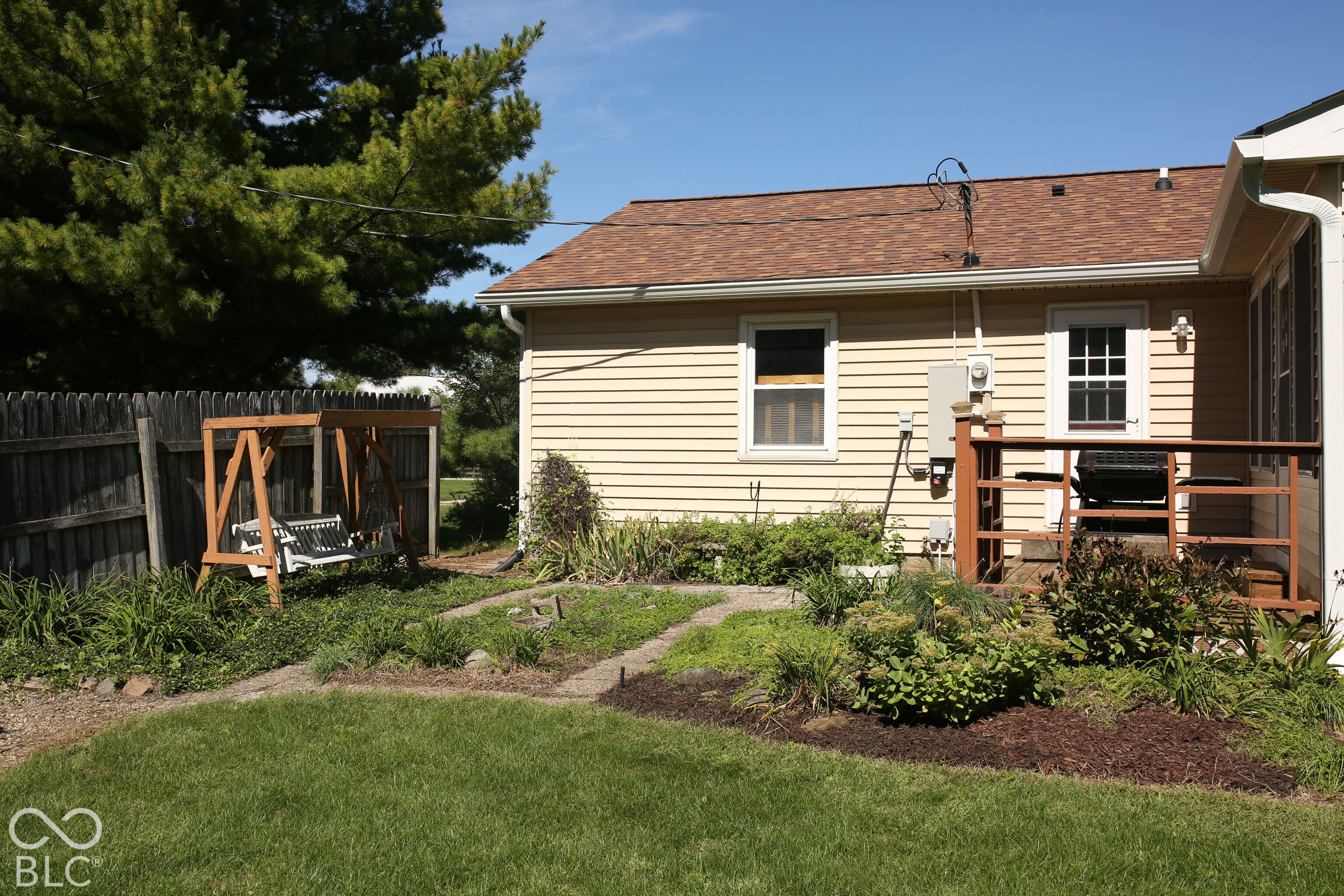 House backyard with a raised deck, grill, wooden swing, and landscaped lawn.