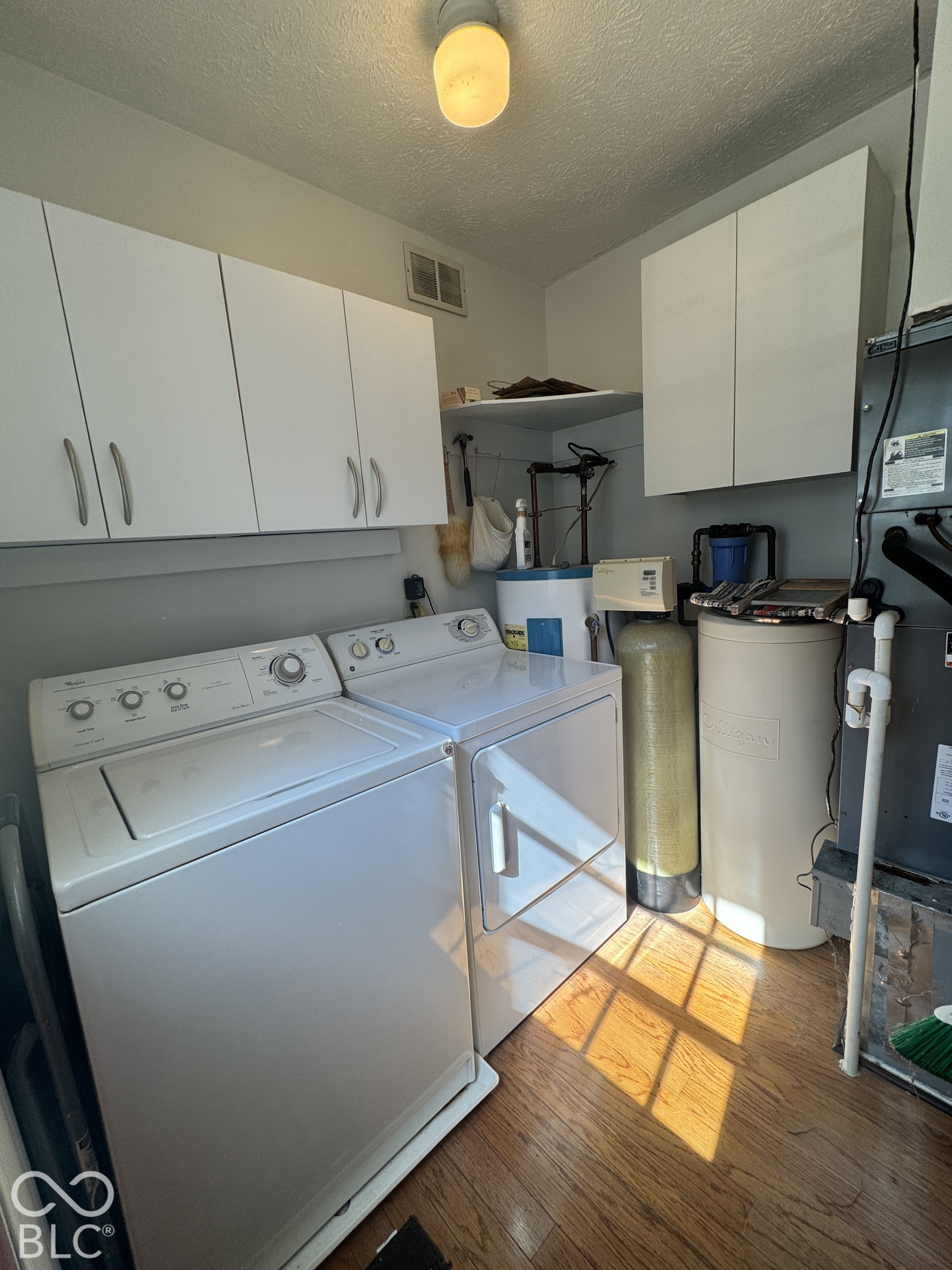 Laundry room with washer and dryer beneath white cabinets, beside a water softener and water heater.