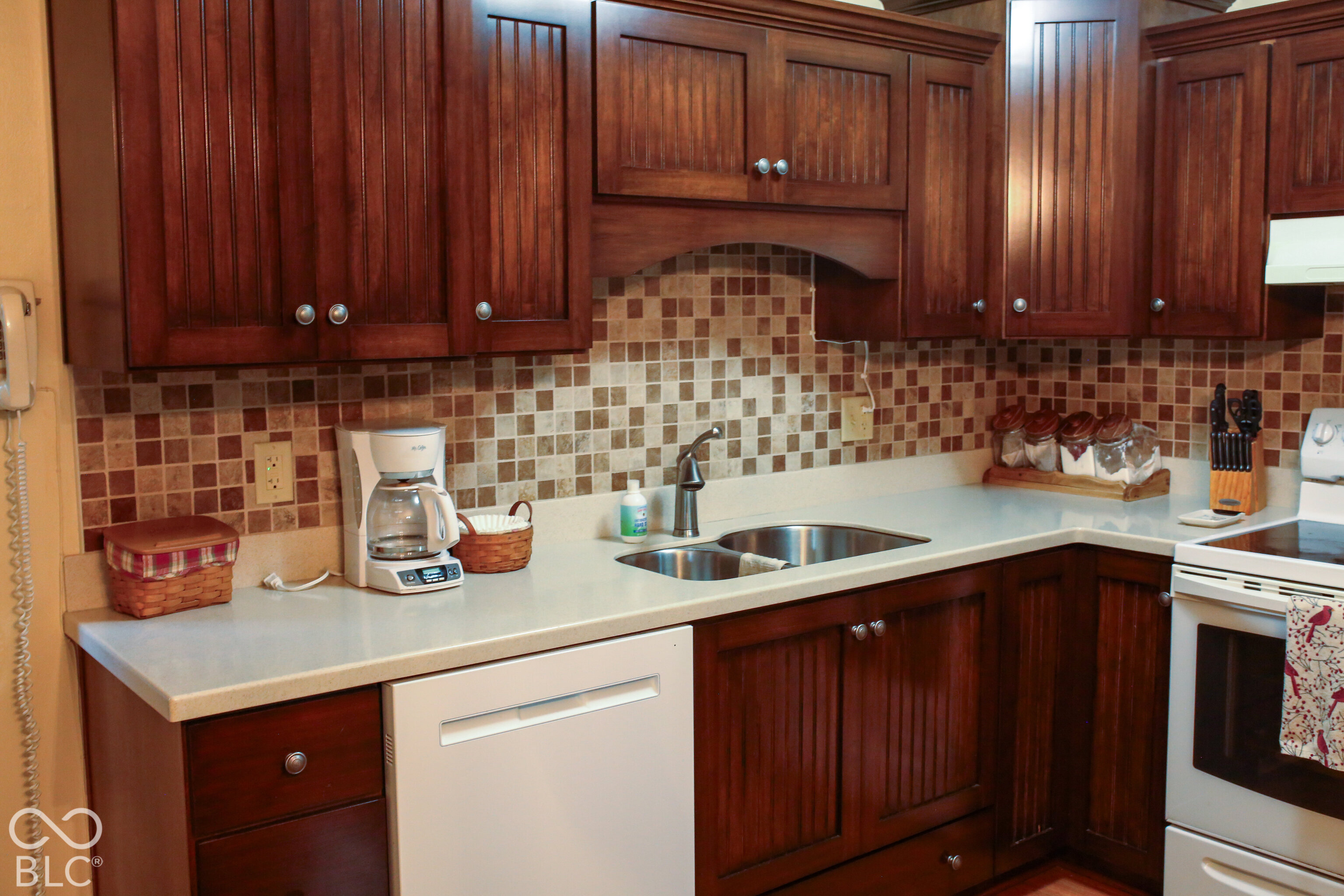 Kitchen with dark wood cabinets, a multicolored tile backsplash, pale counters, and a double-basin sink.