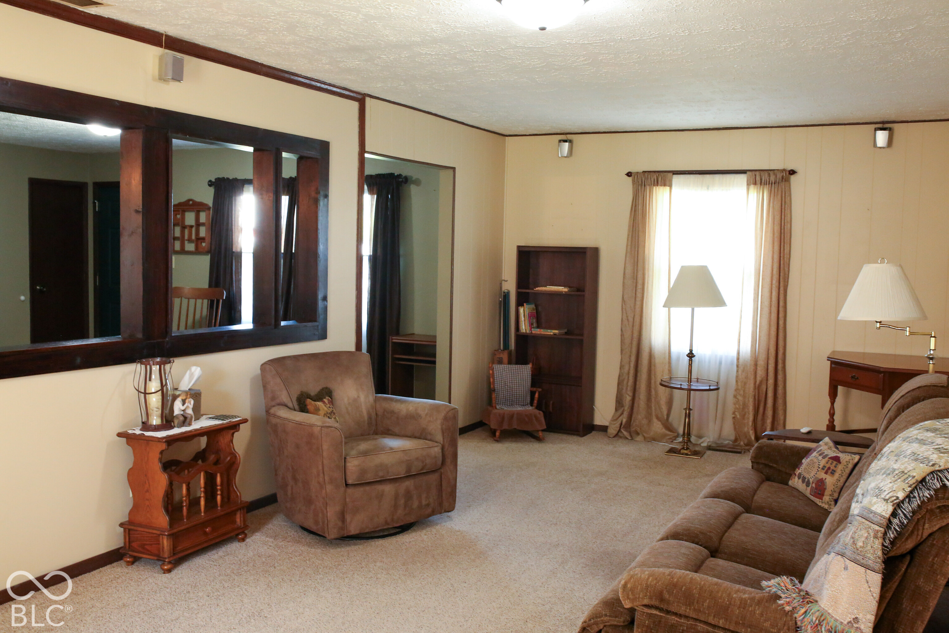 Furnished living room with a brown sofa, armchair, dark wood trim, and bright curtained window.