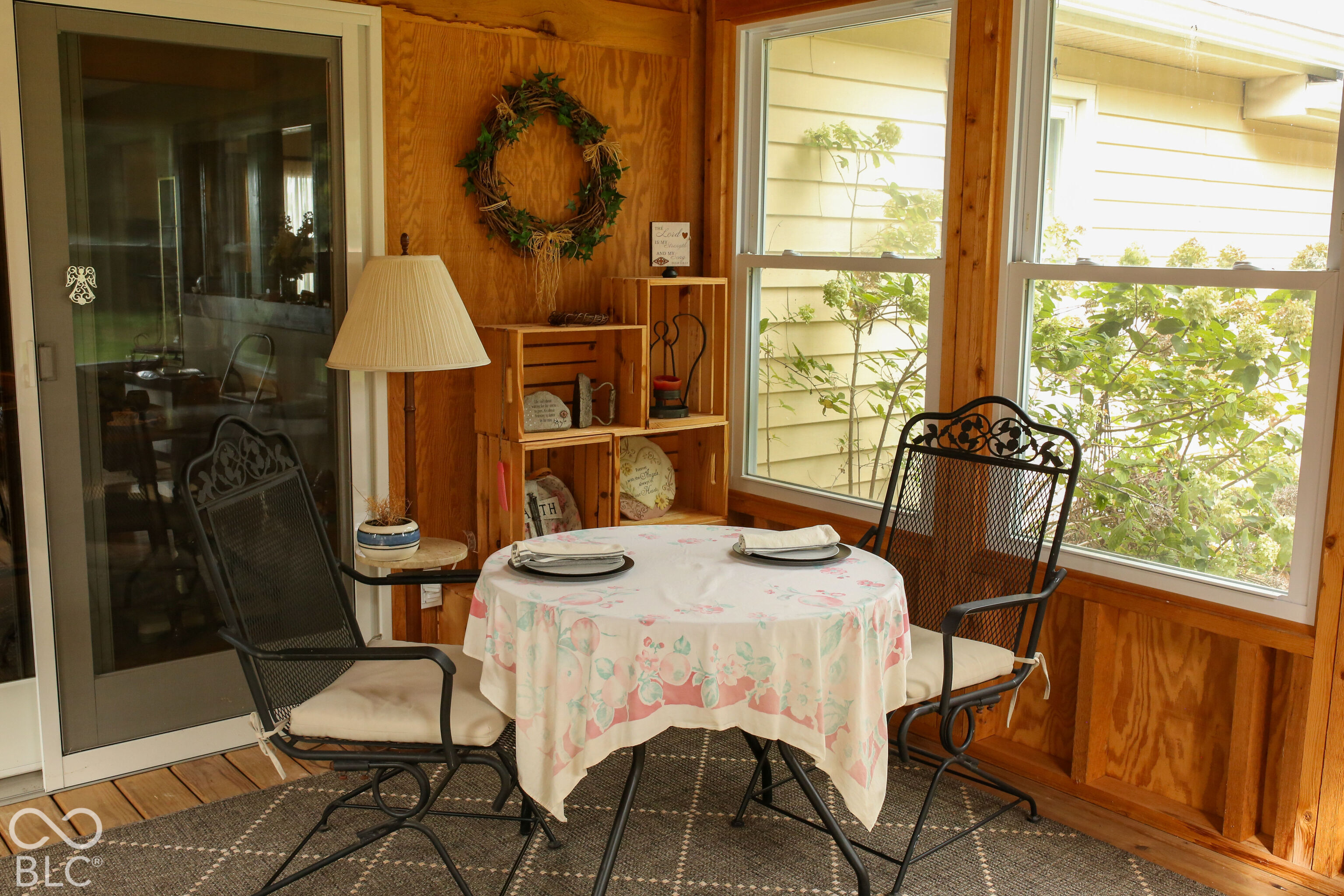 Furnished wood-paneled sunroom with a floral dining table, black metal chairs, and large windows.