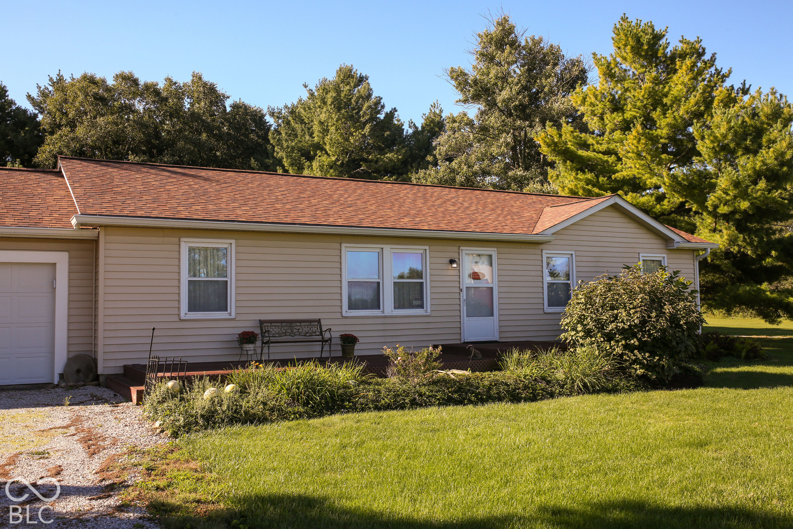Single-story beige house with a red-brown roof, attached garage, landscaped beds, and a green lawn.