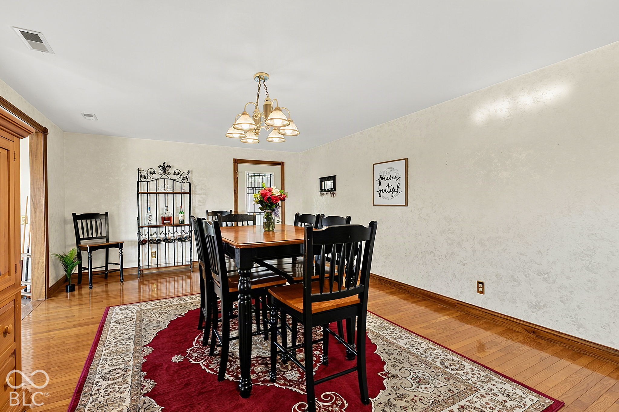 Dining room with a wooden table, black chairs, patterned rug, and chandelier.