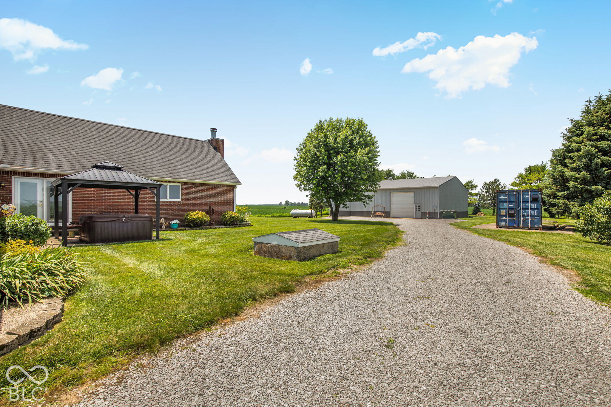 Rural property backyard with a covered hot tub, large metal outbuilding, and gravel driveway.