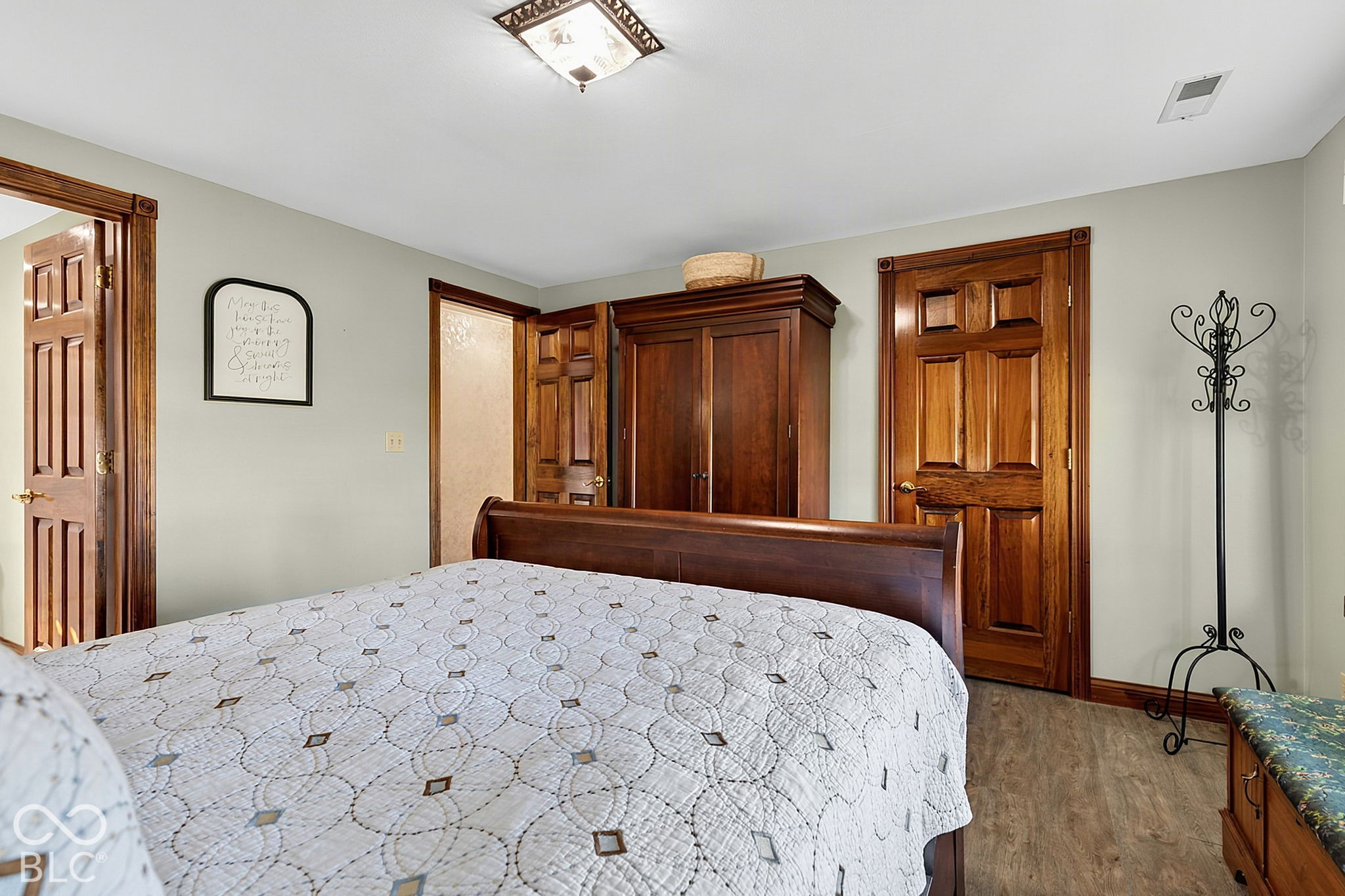 Bedroom with a wooden bed, patterned white quilt, matching wardrobe, and paneled wood doors.