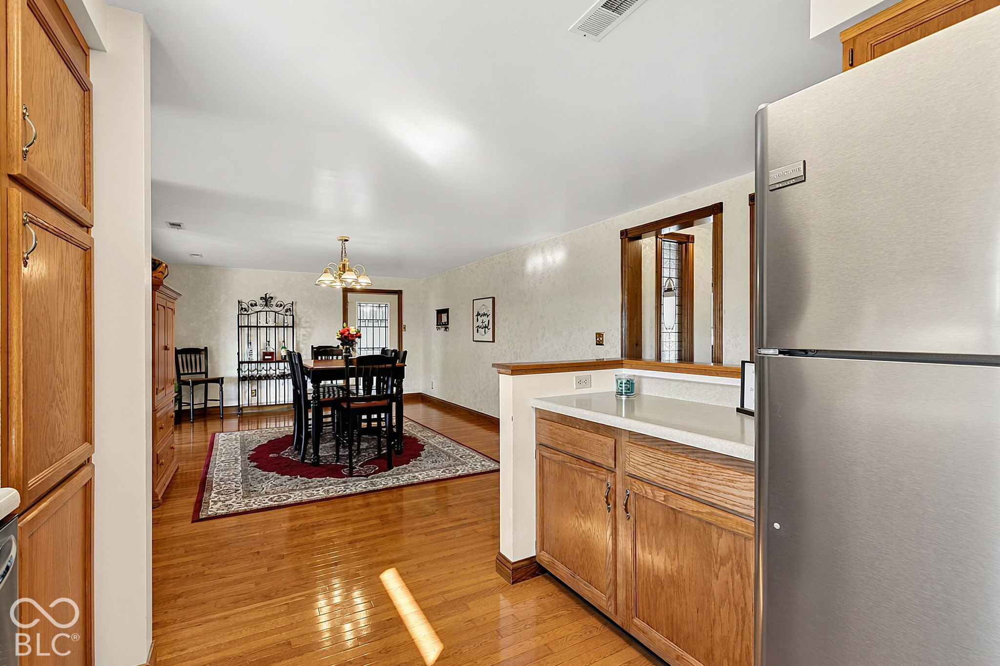 Kitchen opening to a dining area with wood cabinetry, stainless refrigerator, and hardwood floors.