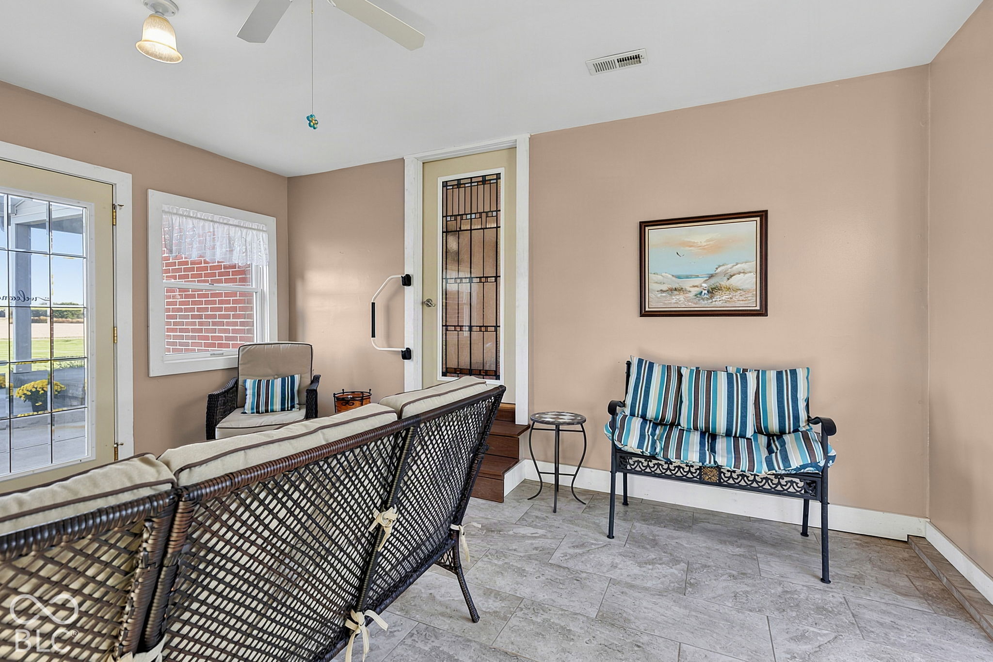 Enclosed sunroom with wicker seating, striped cushions, and a glass-paneled door.