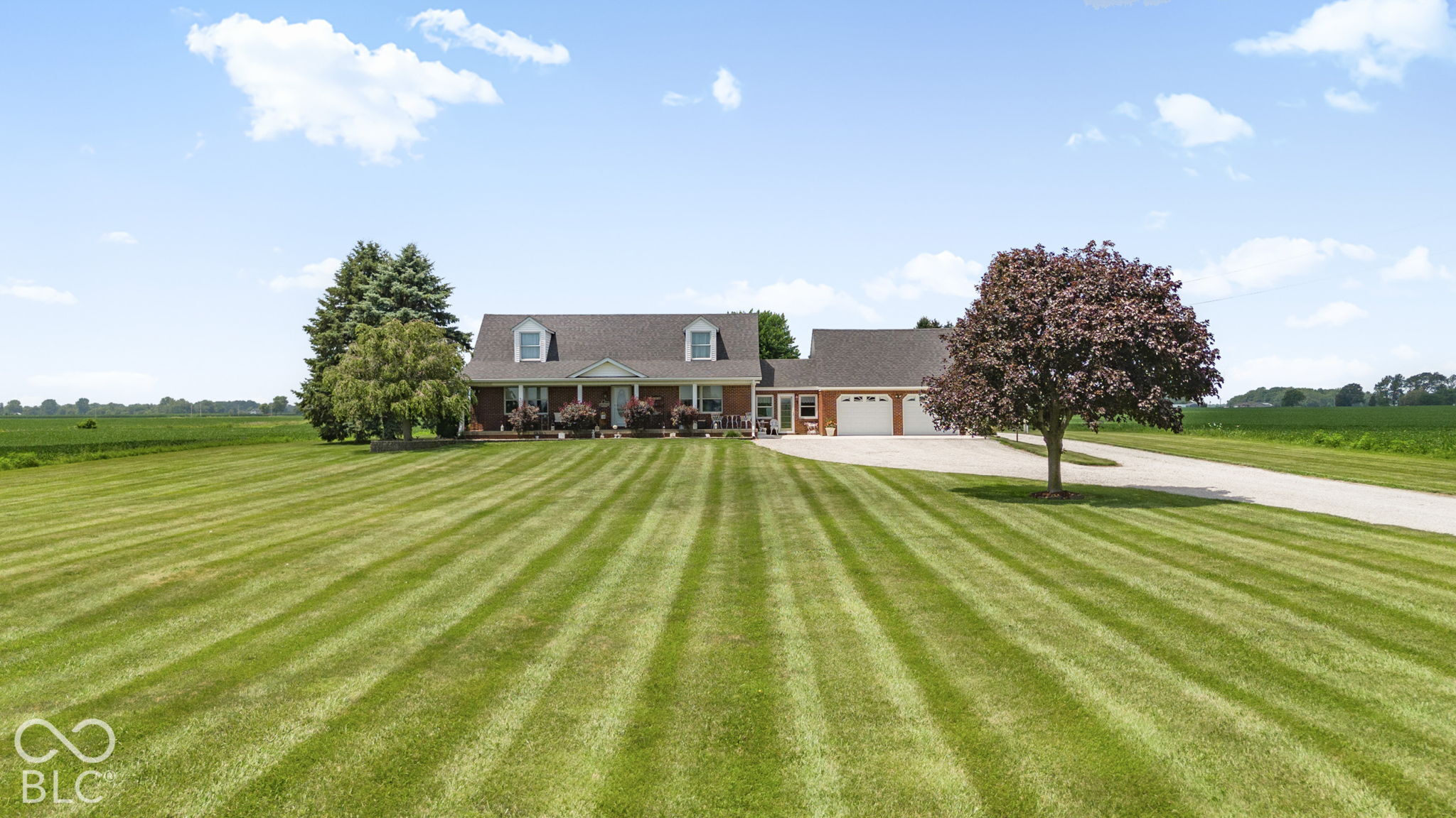 Brick home with attached garage, striped lawn, mature trees, and open farmland.