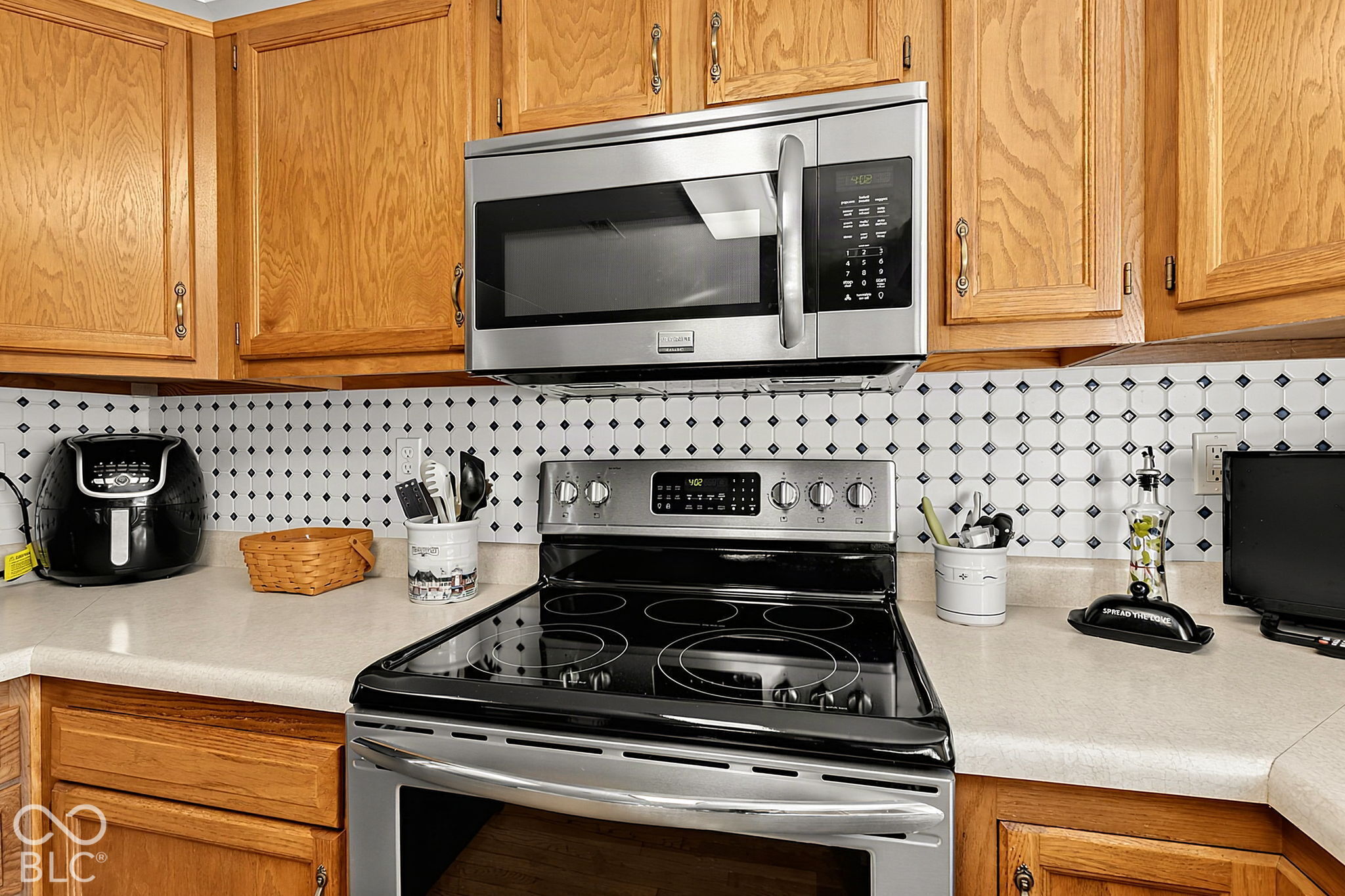 Kitchen with wood cabinets, a patterned tile backsplash, and stainless steel microwave above a black range.