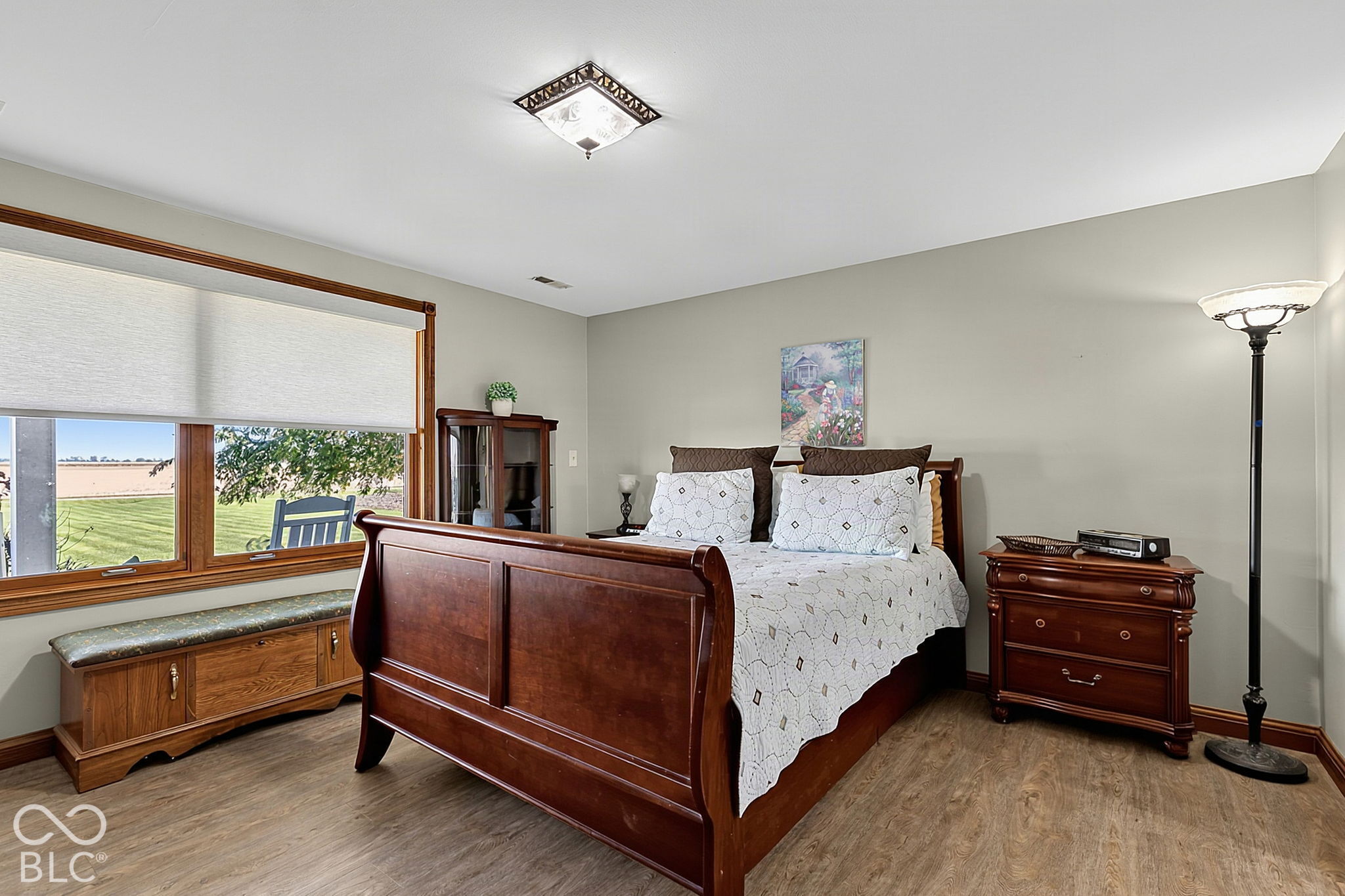 Bedroom with a dark wood four-poster bed and a large window overlooking open fields.