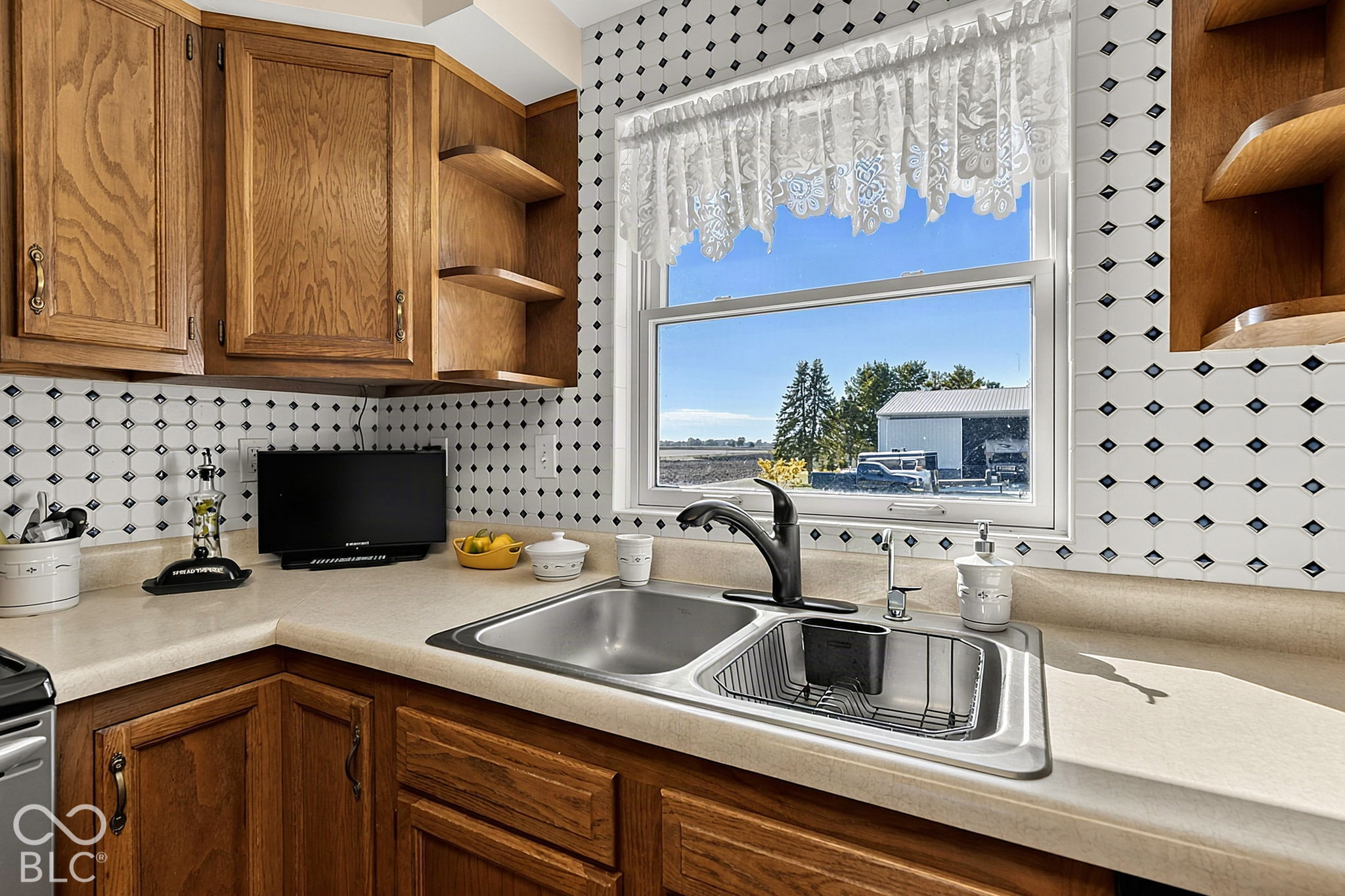 Kitchen with oak cabinets, a double-basin sink, and black-and-white diamond tile around the window.
