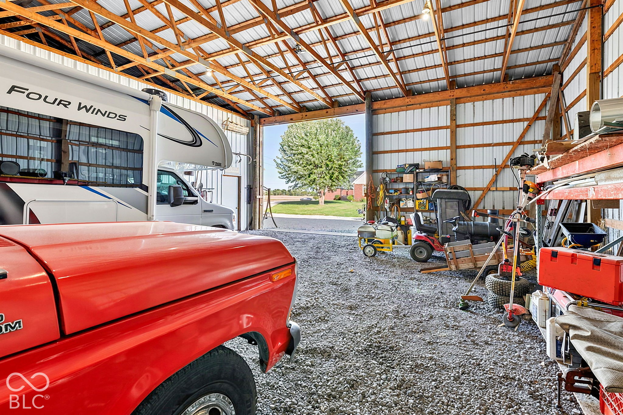 Large barn workshop with exposed timber trusses, a motorhome, red truck, and riding mower.