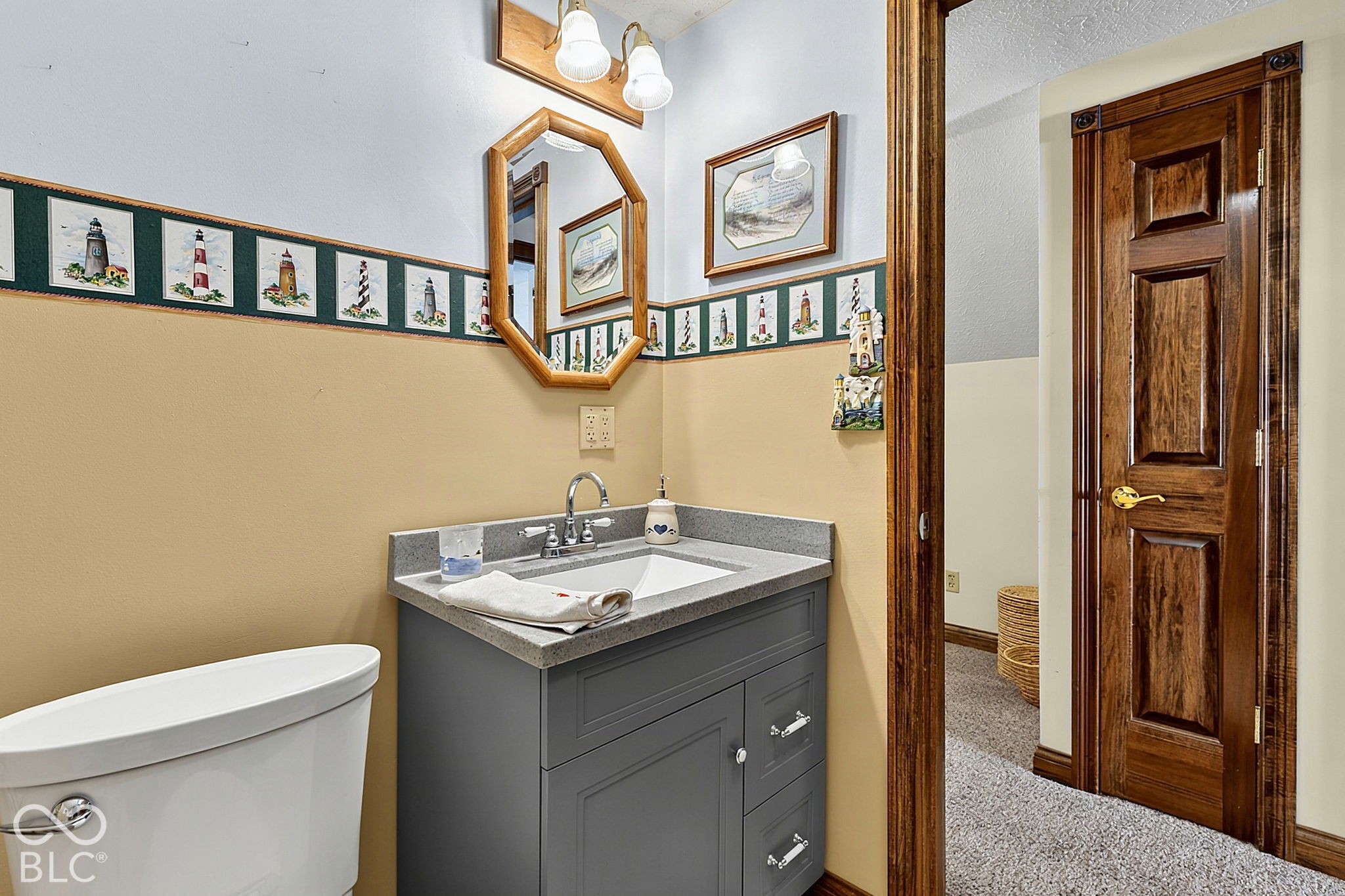Bathroom with gray vanity, white sink and toilet, lighthouse border, and dark wood paneled door.