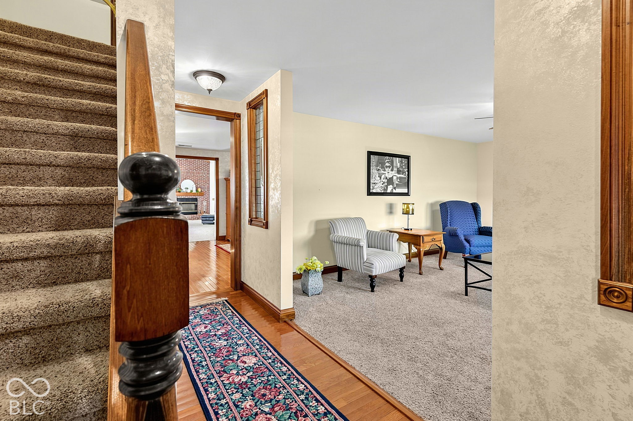 Living room beside the entry hall and carpeted staircase, with striped chairs, a blue armchair, and a floral runner.