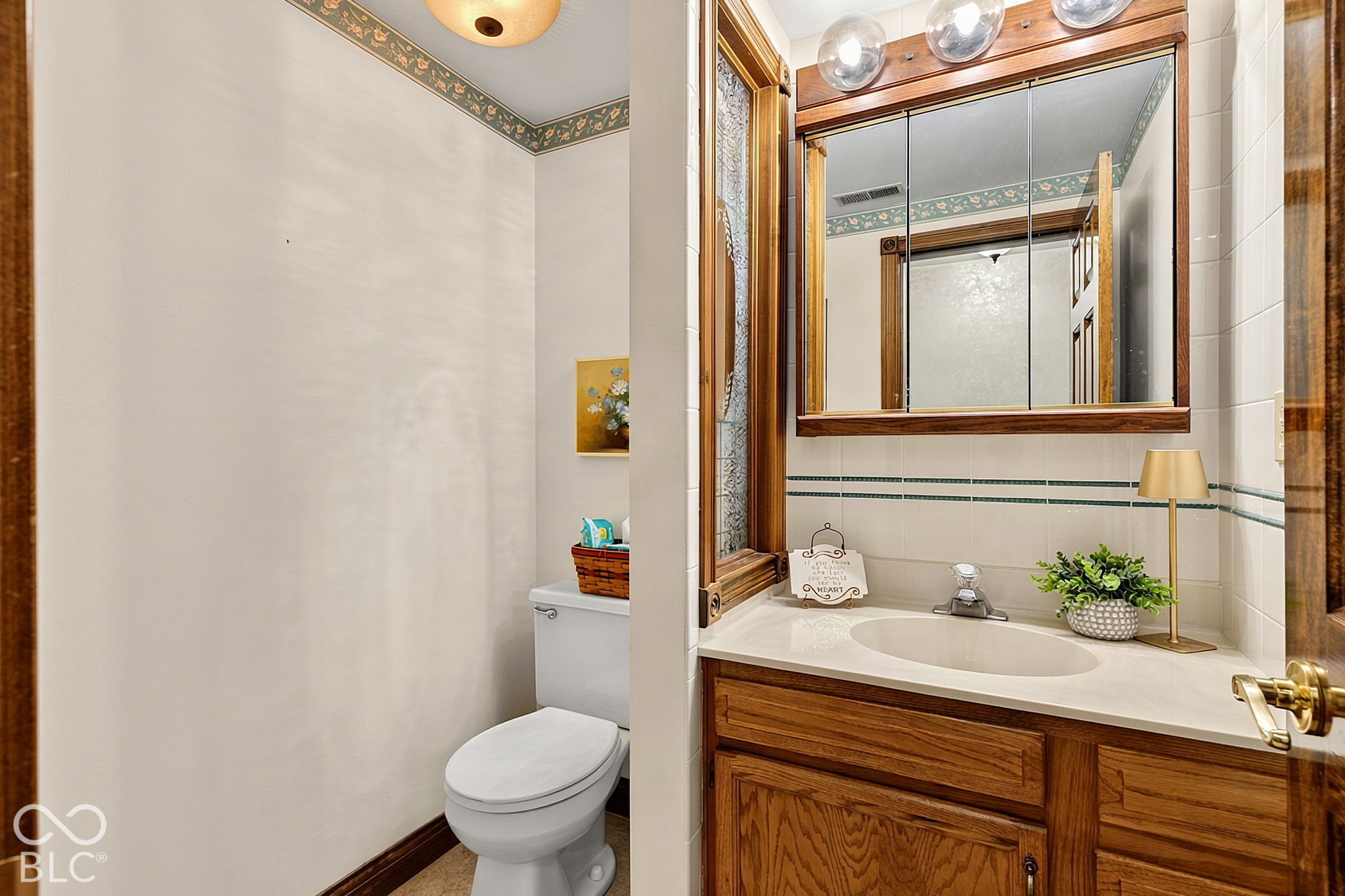 Bathroom with a wood vanity, mirrored cabinet, tiled walls, and toilet.
