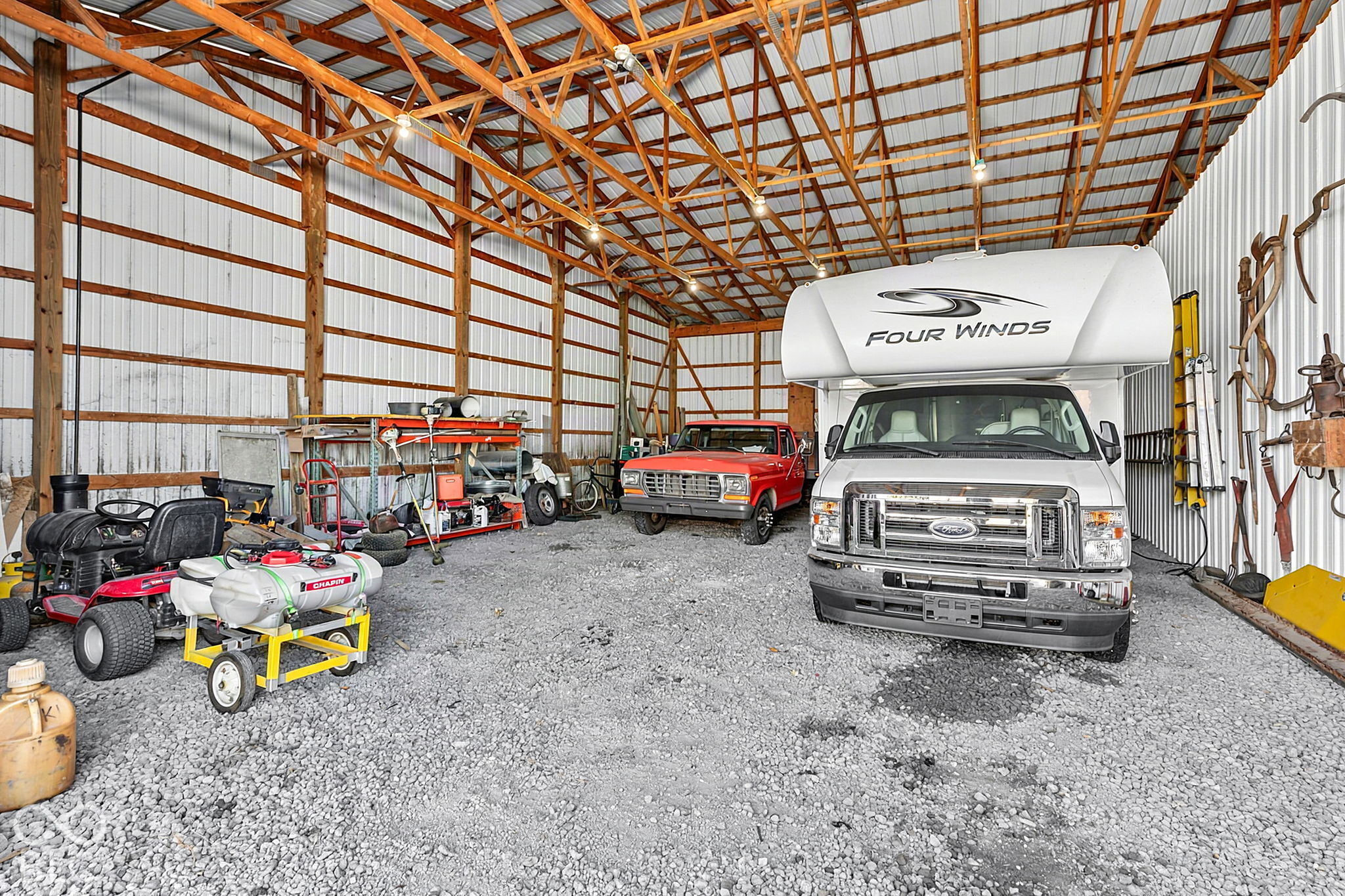Pole barn interior with a motorhome, red pickup, lawn equipment, and gravel floor.
