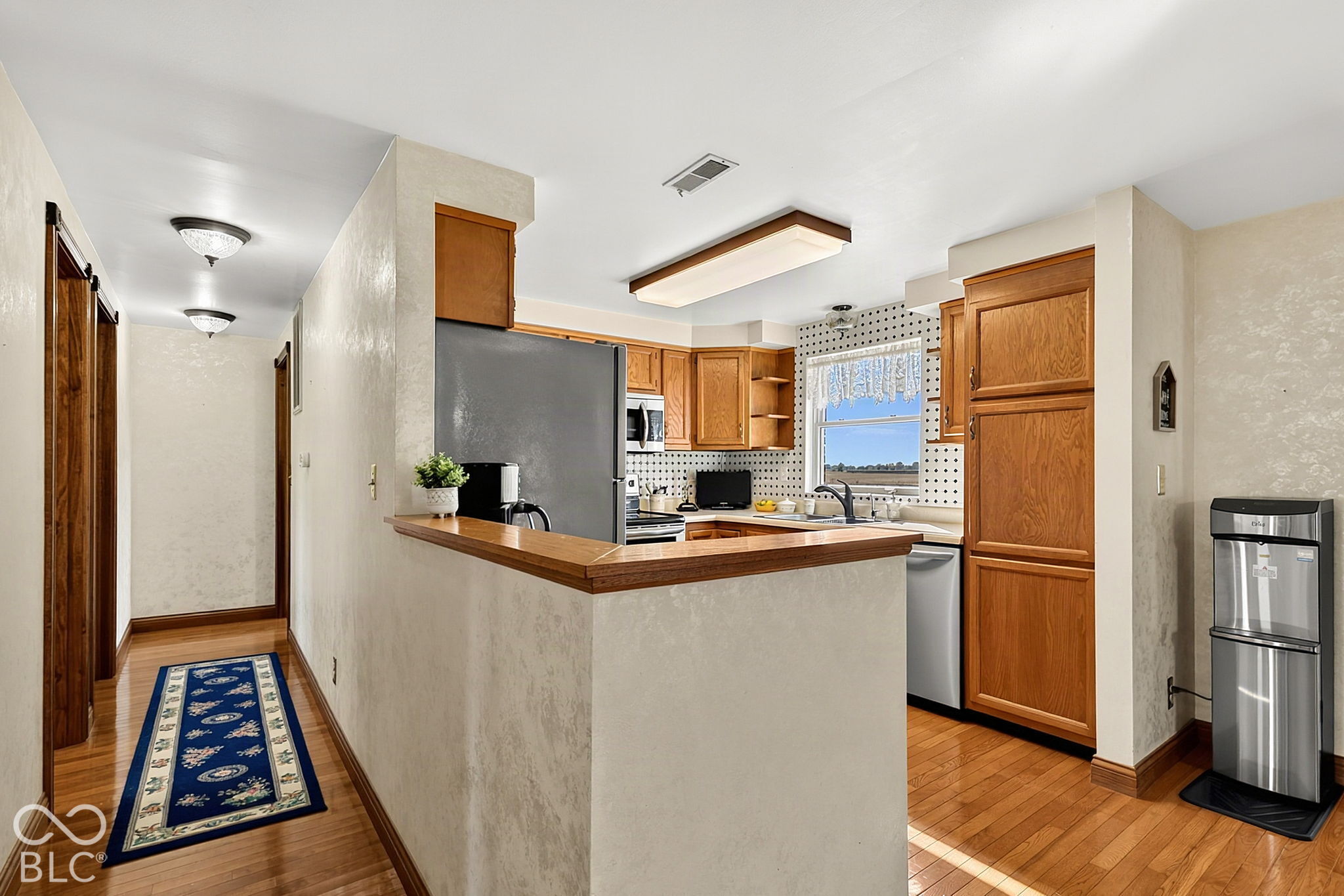 Kitchen with warm wood cabinets, hardwood floors, and a raised peninsula counter beside the hallway.