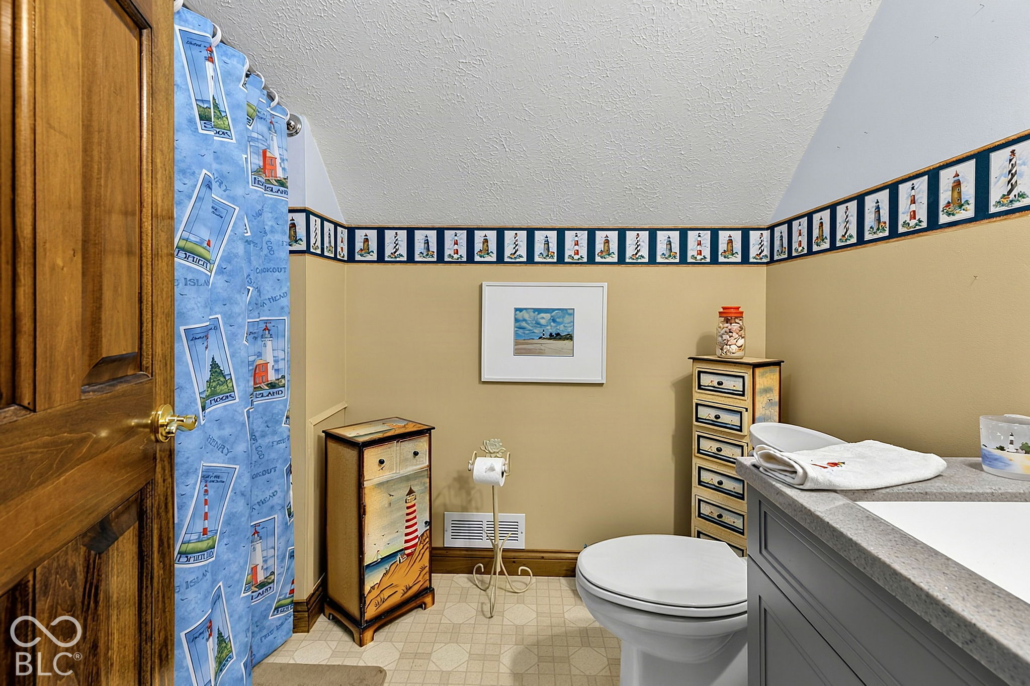 Bathroom with a lighthouse-patterned shower curtain and coordinating nautical decor.