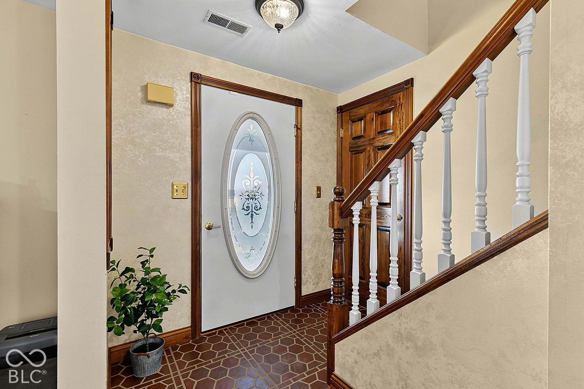 Entry foyer with oval-glass front door, patterned tile floor, and wood staircase with white balusters.