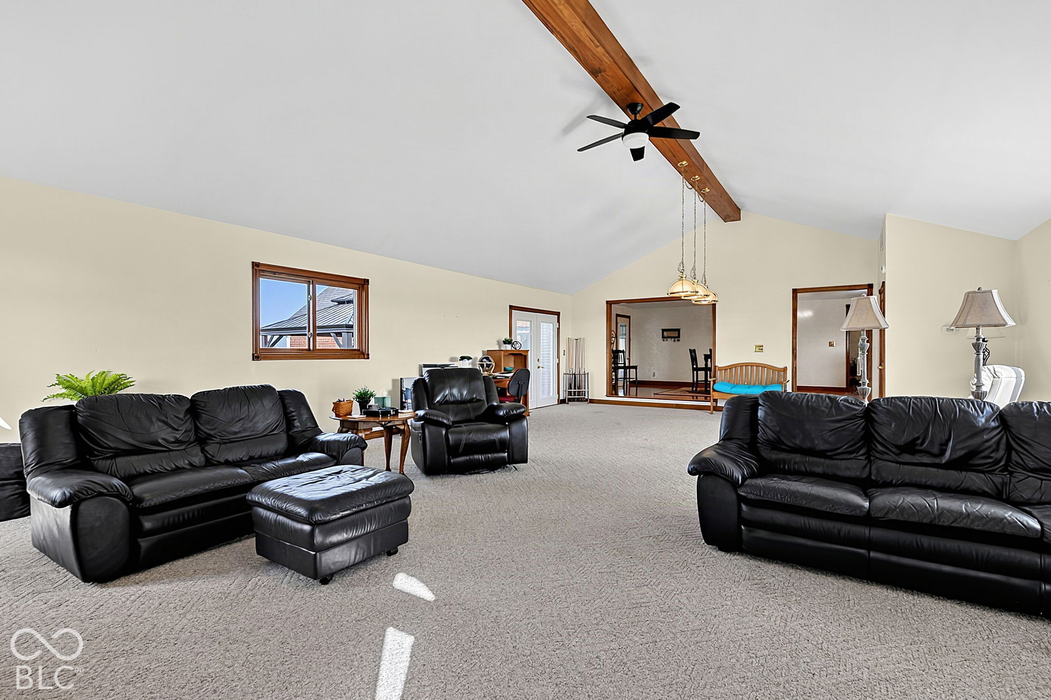 Furnished living room with black leather seating, gray carpet, and a vaulted ceiling with a wood beam.