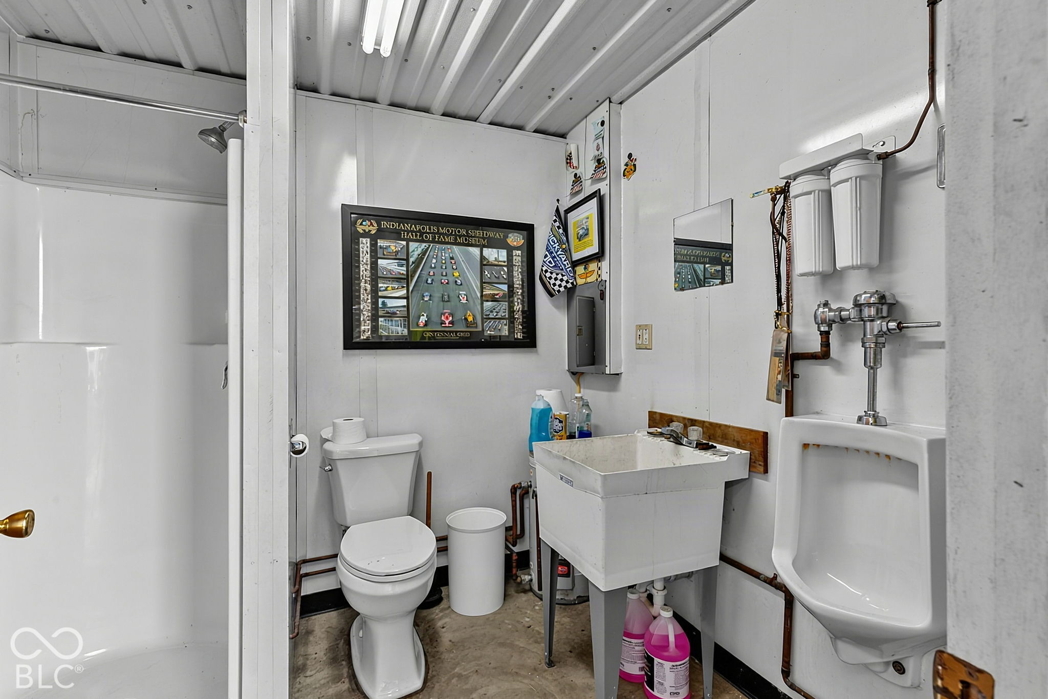 Utility bathroom with a toilet, urinal, and deep sink beneath a framed Indianapolis Motor Speedway display.