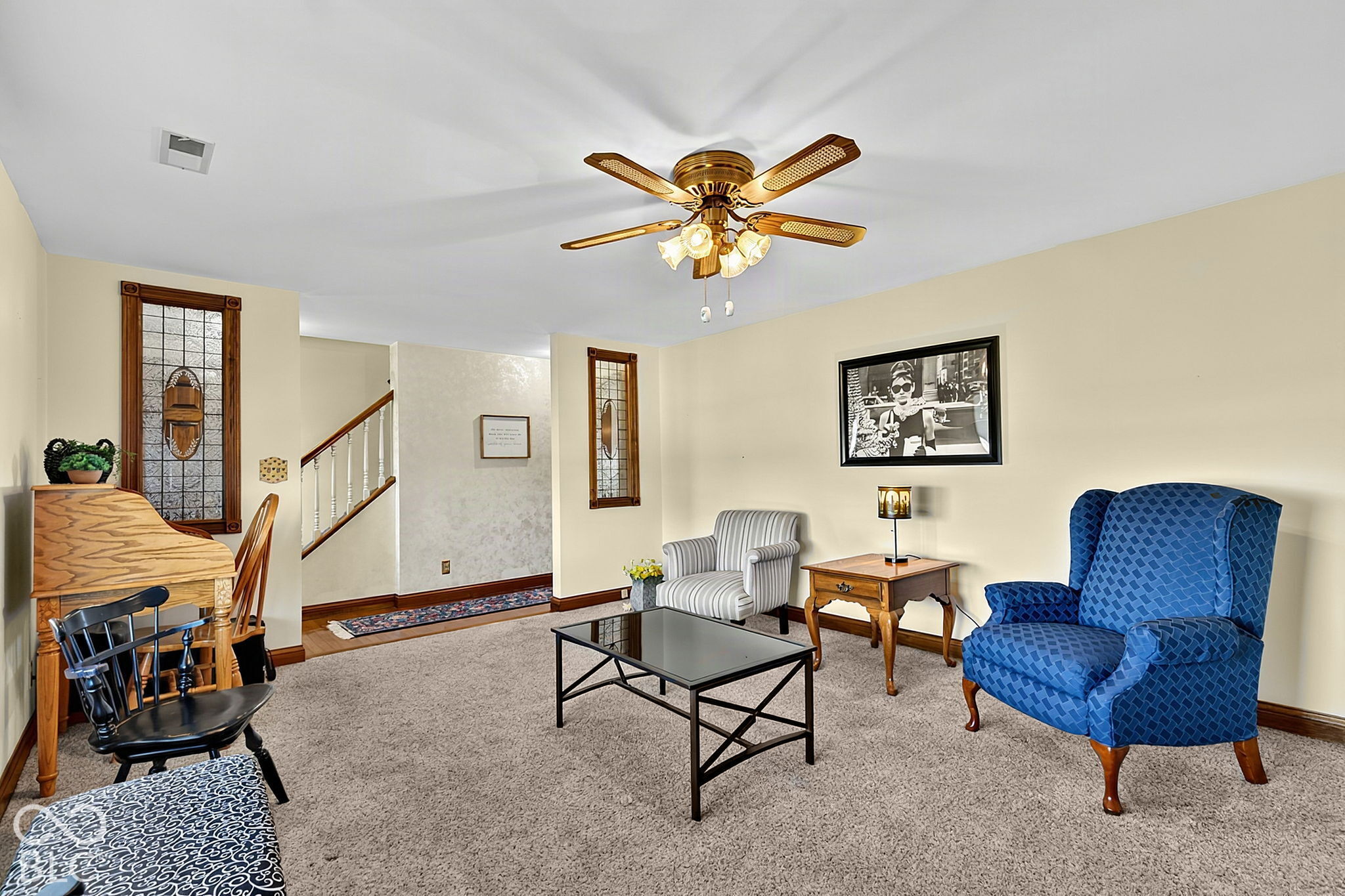 Living room with a blue patterned armchair, striped chair, glass-top coffee table, and staircase.