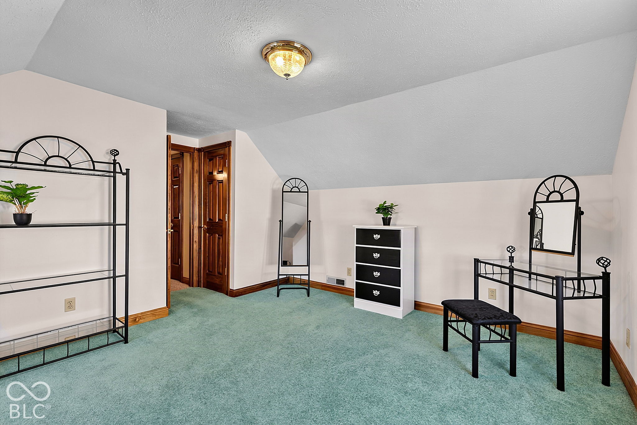Carpeted bedroom with a sloped ceiling, black metal dressing table and mirrors, and dark wood doors.