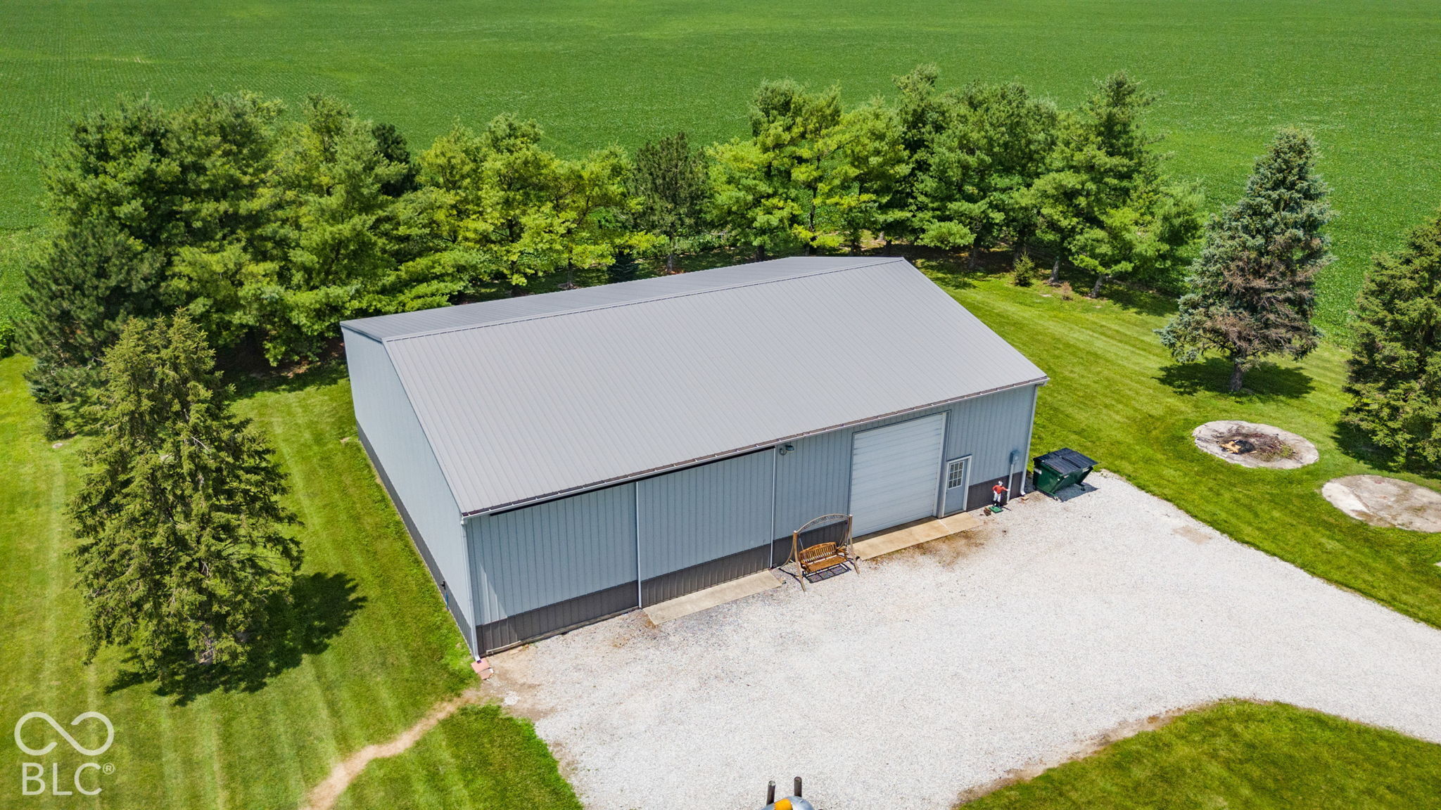 Large gray metal outbuilding with a gravel driveway, lawn, and mature trees, seen from above.
