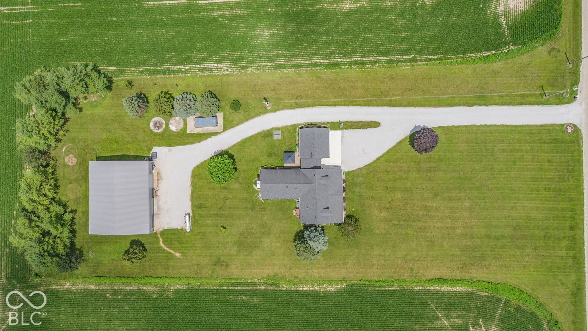 Aerial view of a rural home and detached outbuilding surrounded by lawn and crop fields.