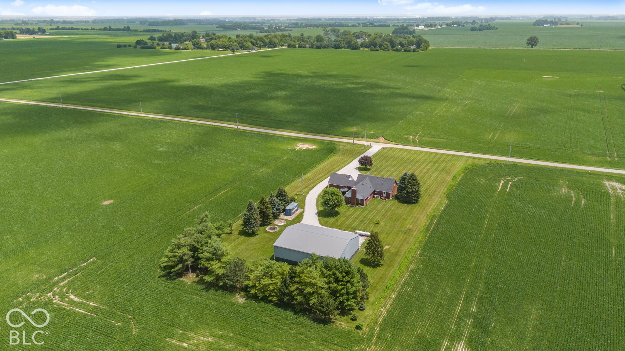 Aerial view of a brick country home, detached outbuilding, and mowed yard surrounded by crop fields.
