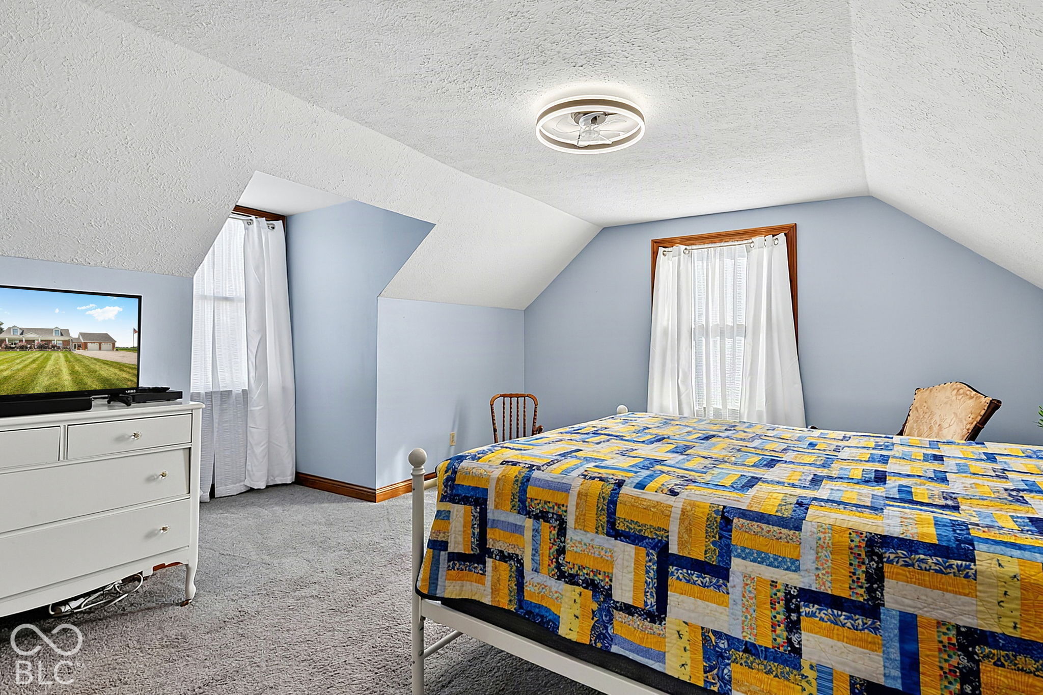Furnished bedroom with a blue and yellow patchwork quilt beneath a sloped ceiling.