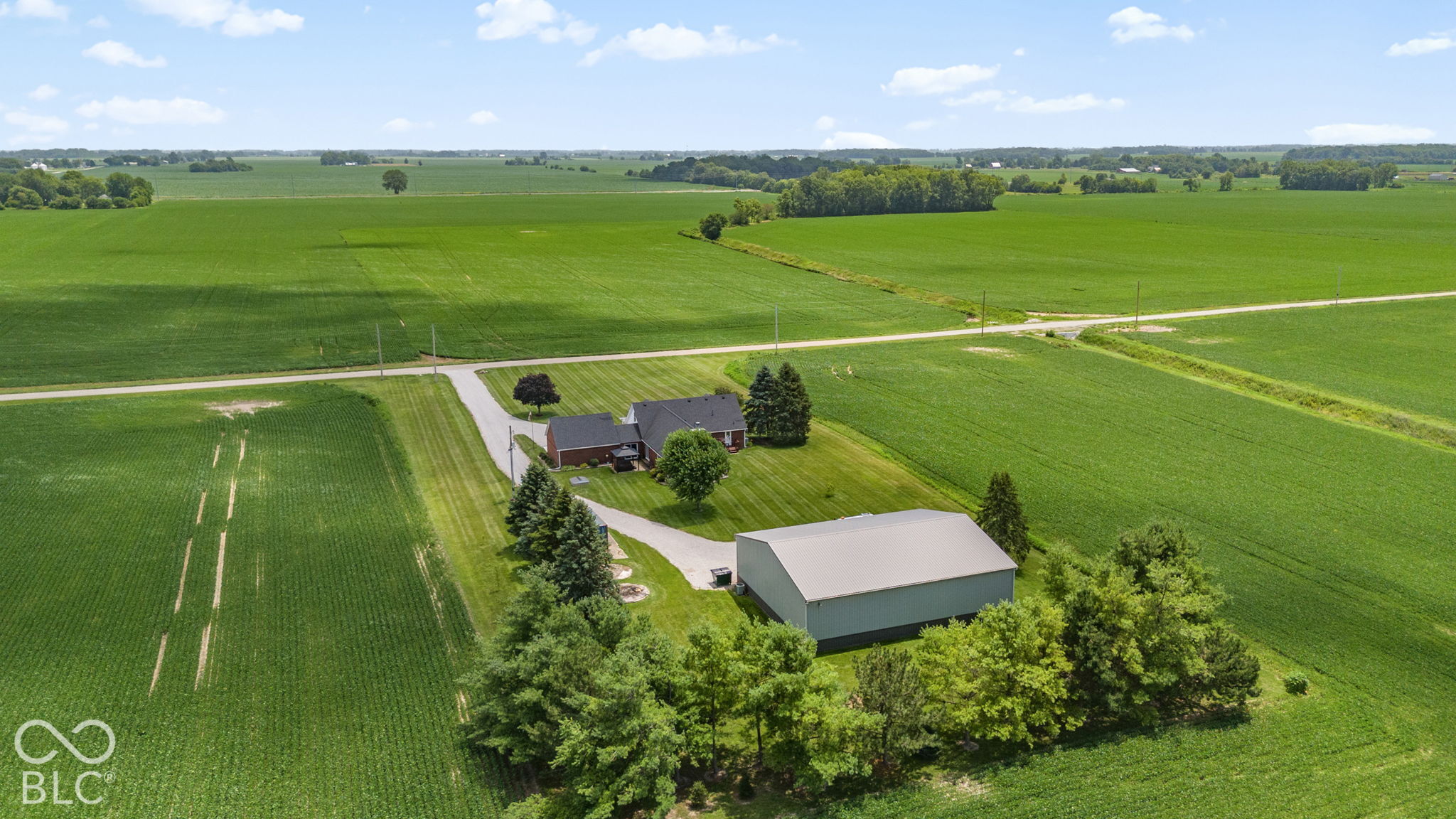 Aerial view of a brick farmhouse and large barn amid expansive green fields.
