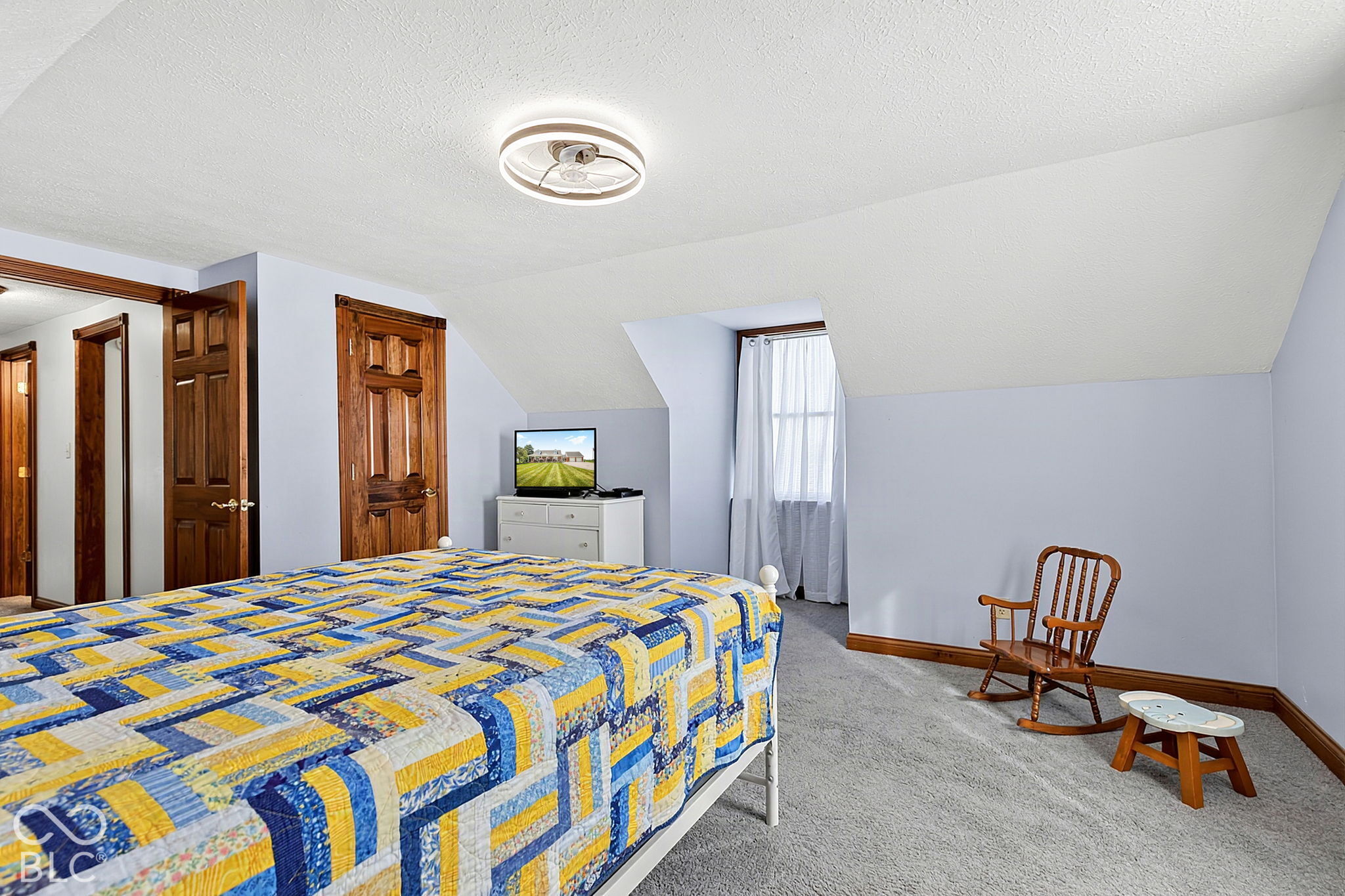 Furnished bedroom with a colorful patchwork quilt, sloped ceiling, and wooden rocking chair.