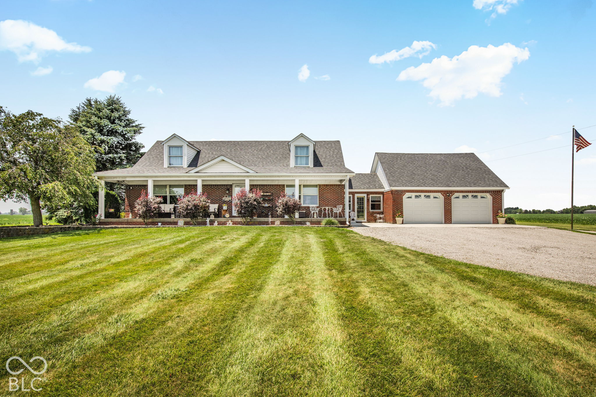 Red-brick home with a covered porch, attached two-car garage, and broad lawn.