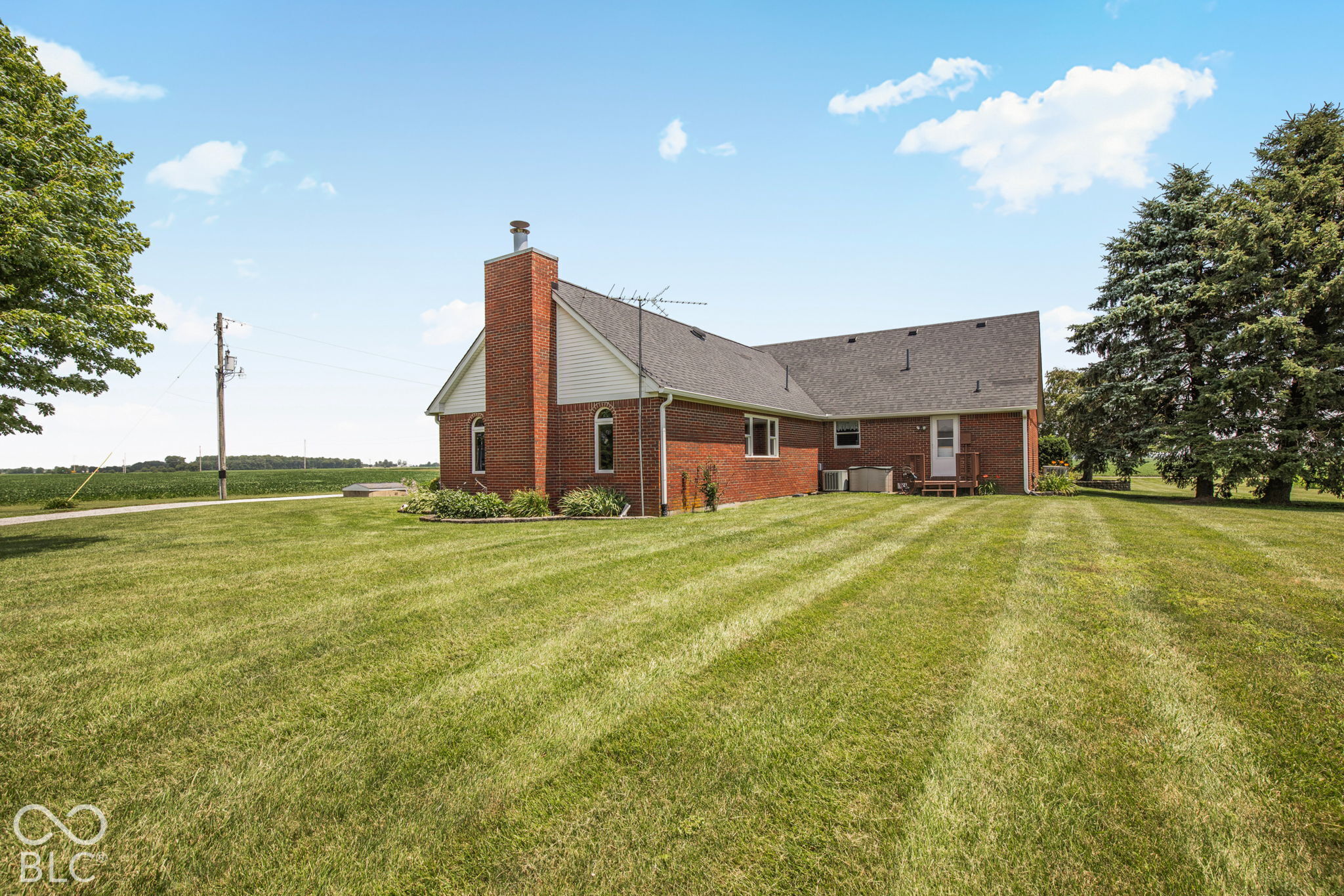 Red-brick house with a tall chimney and broad mowed lawn beside open farmland.