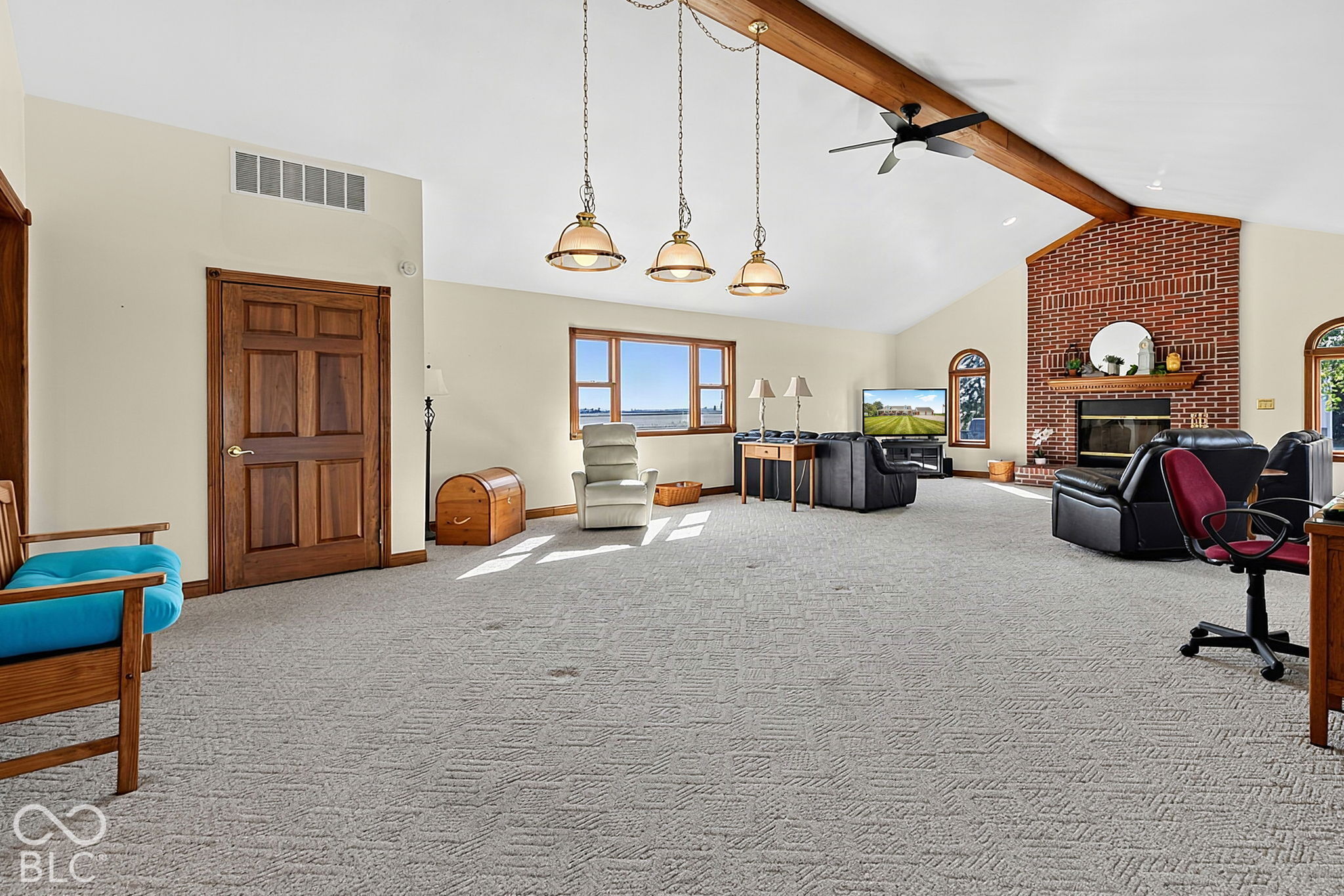 Living room with a vaulted ceiling, exposed beam, brick fireplace, and windows overlooking water.